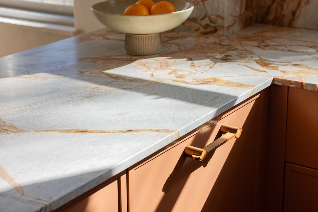 A marble kitchen countertop with a bowl of oranges on a pedestal in the background