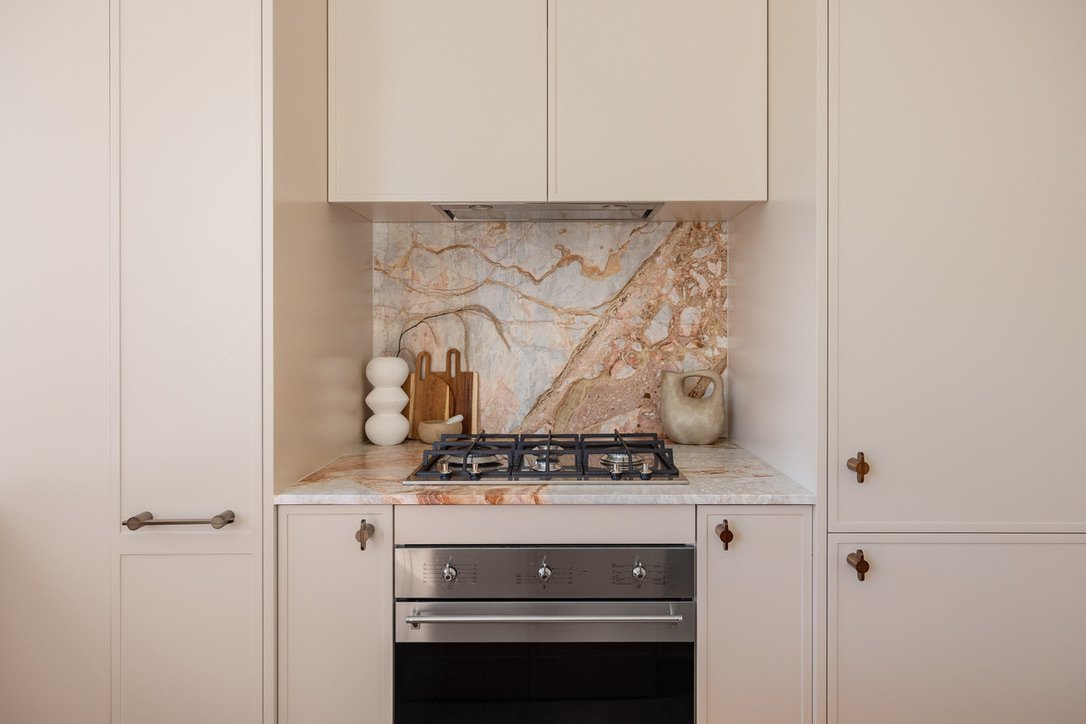 Kitchen with beige cabinets, marble backsplash, stovetop, oven, and decorative vases.