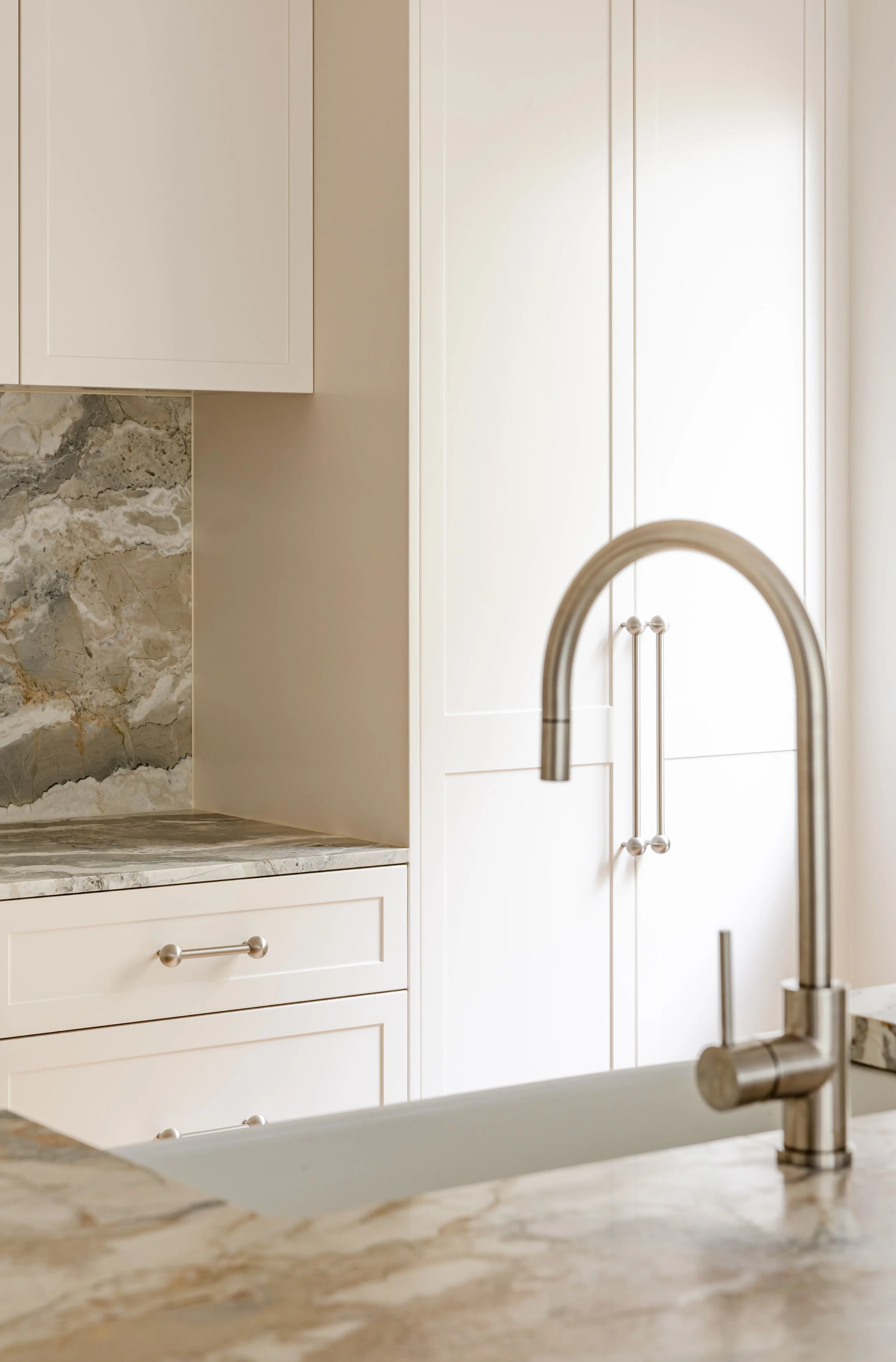 Modern kitchen with a stainless steel faucet, white cabinetry, and marble countertops with a textured backsplash.