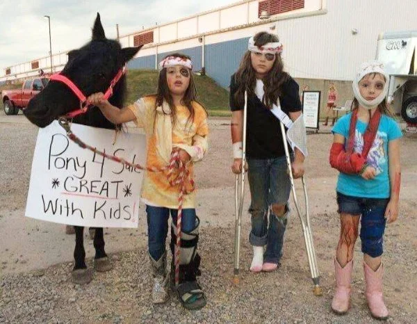 Three young girls standing beside a small horse with a sign that reads 'Pony Rides - Great with Kids.' The girls are wearing helmets, and one girl has crutches, indicating they are participating in a pony ride event.