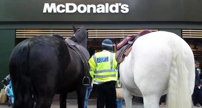 A police officer stands between two horses outside a McDonald's restaurant.