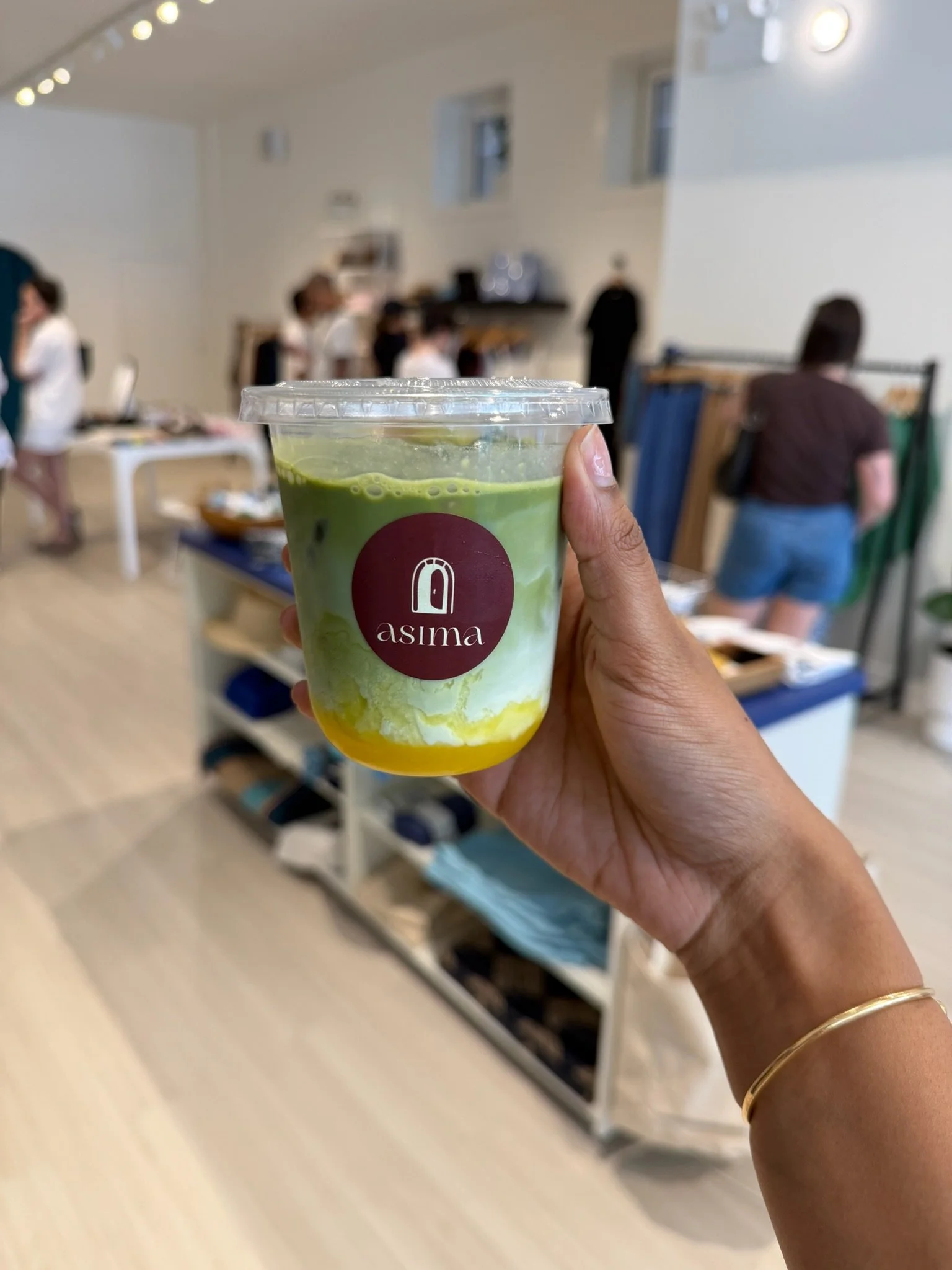 Person holding a green drink with the label 'asima' in a store or café.
