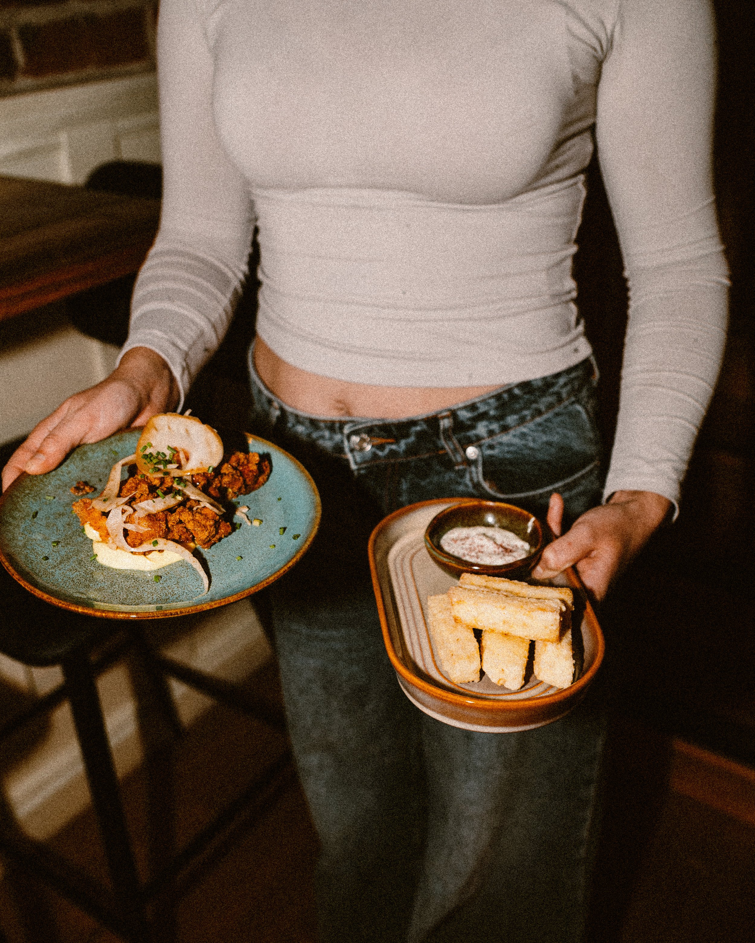 A person holding two plates of food, with one plate containing tacos and the other with grilled cheese sandwiches and a dipping sauce.