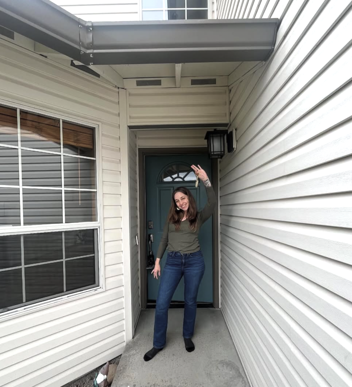 A homebuyer client smiling in front of her new house with keys after Lou Chain helped her become a homeowner