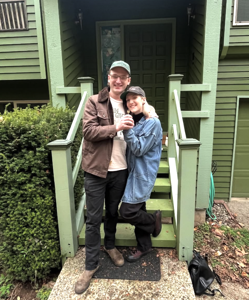 A couple smiles in front of their new home after their home purchase successfully closed with Lou Chain.