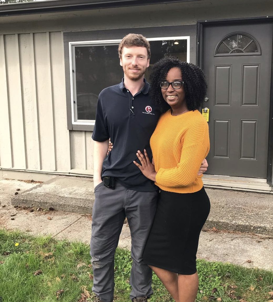A couple who were homebuyer clients of Lou Chain, stand in front of their home and they smile