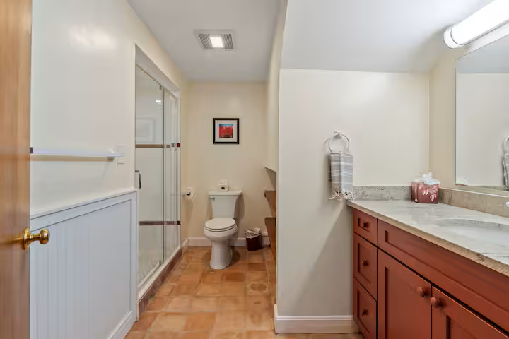 Bathroom with a shower enclosure, toilet, wooden cabinet with a marble countertop, and a mirror
