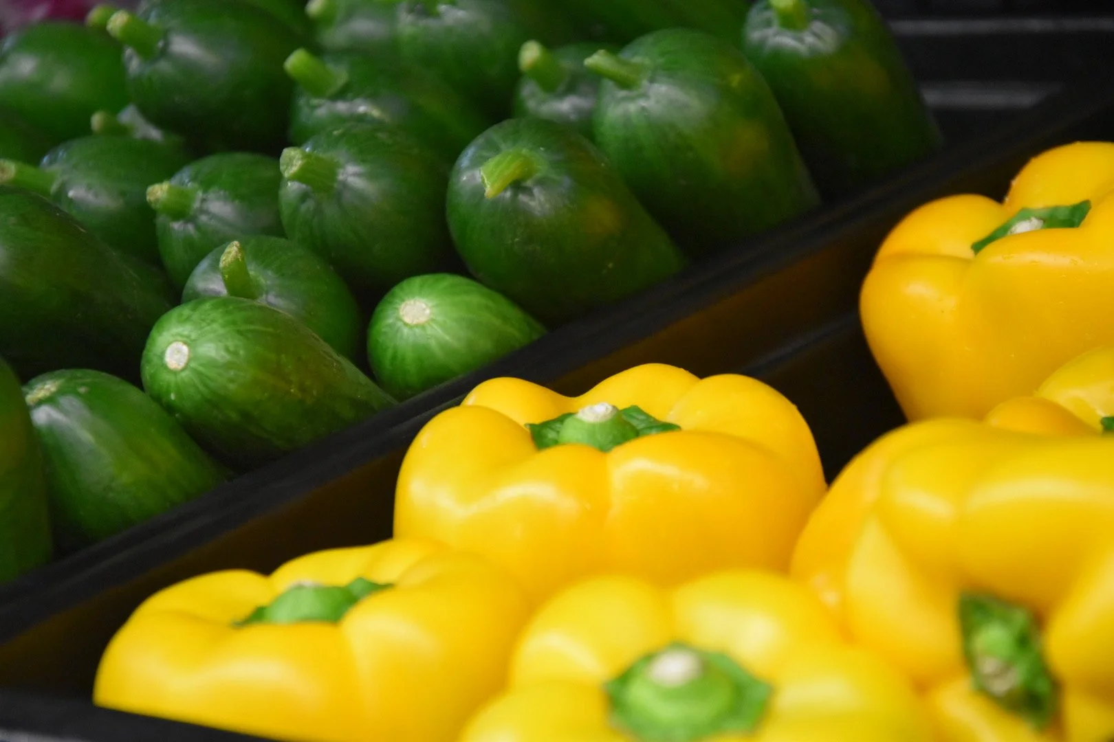 Green and yellow bell peppers arranged on display at a grocery store.