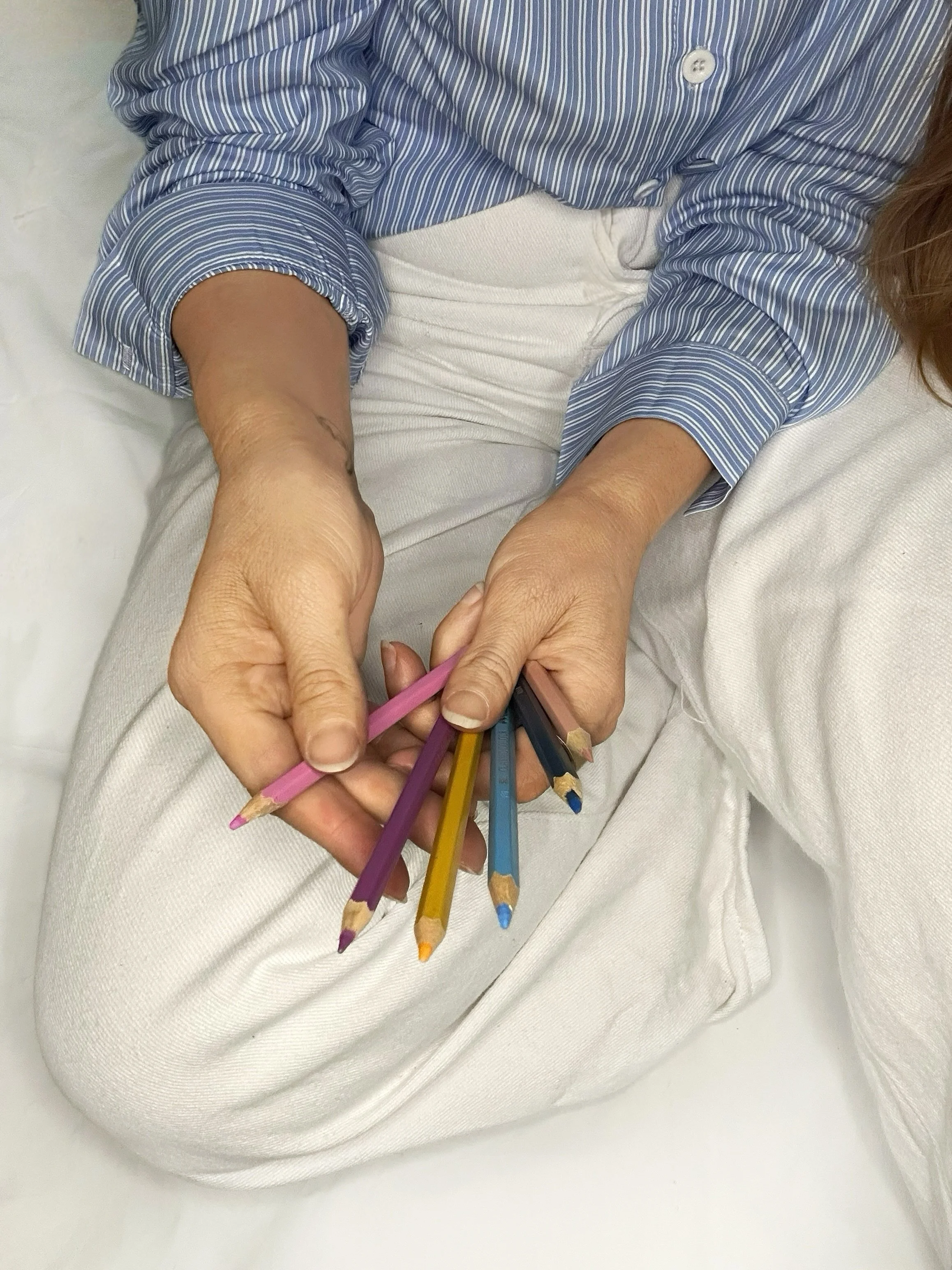 Person sitting on a bed holding multiple colored pencils in their hands