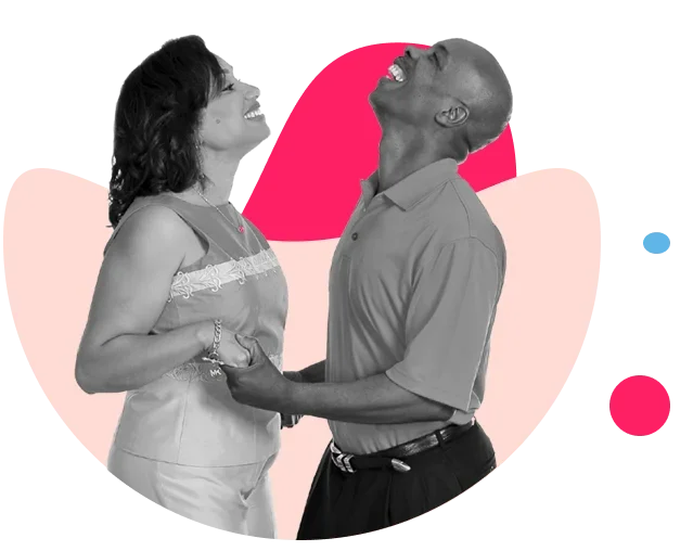 A black and white photo of a joyful couple holding hands and laughing together, with a pink heart in the background.