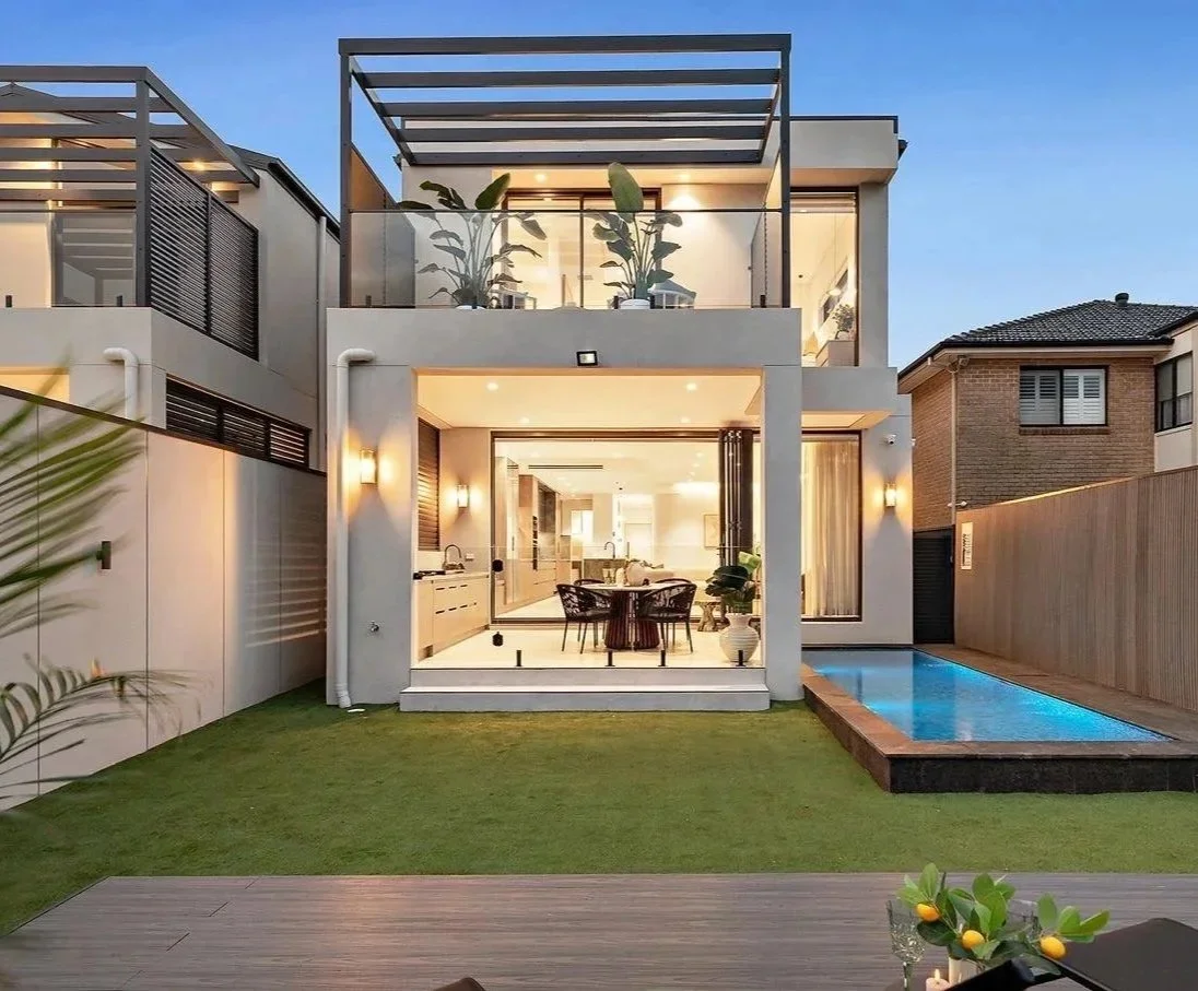 Modern two-story house with an outdoor patio, garden, and swimming pool at dusk.