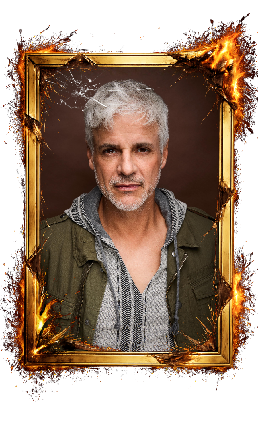A mature man with gray hair and a serious expression, wearing a gray hoodie and a green jacket, is inside a fiery, broken picture frame against a dark background.