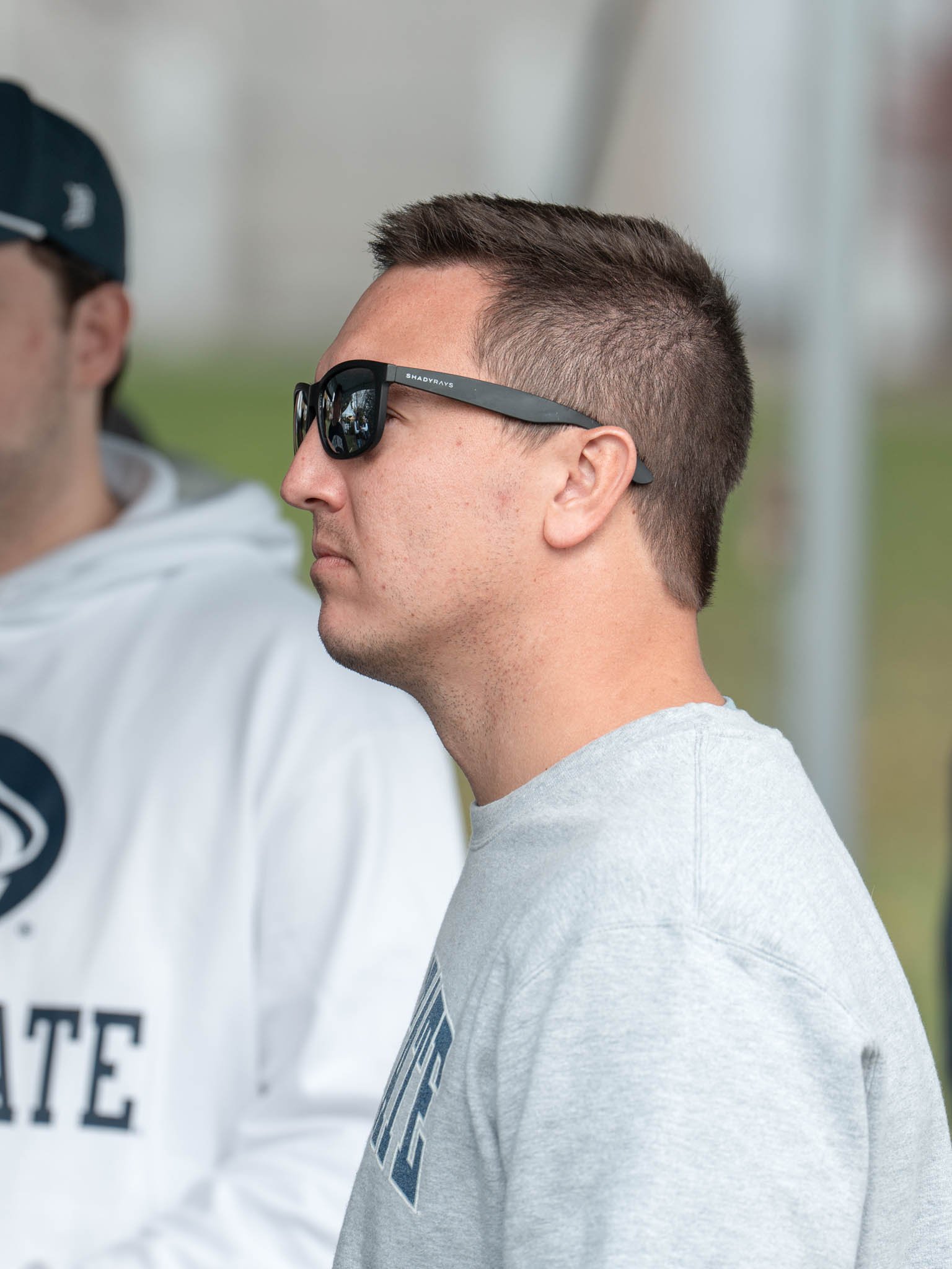 A man in profile wearing sunglasses and a light gray T-shirt.