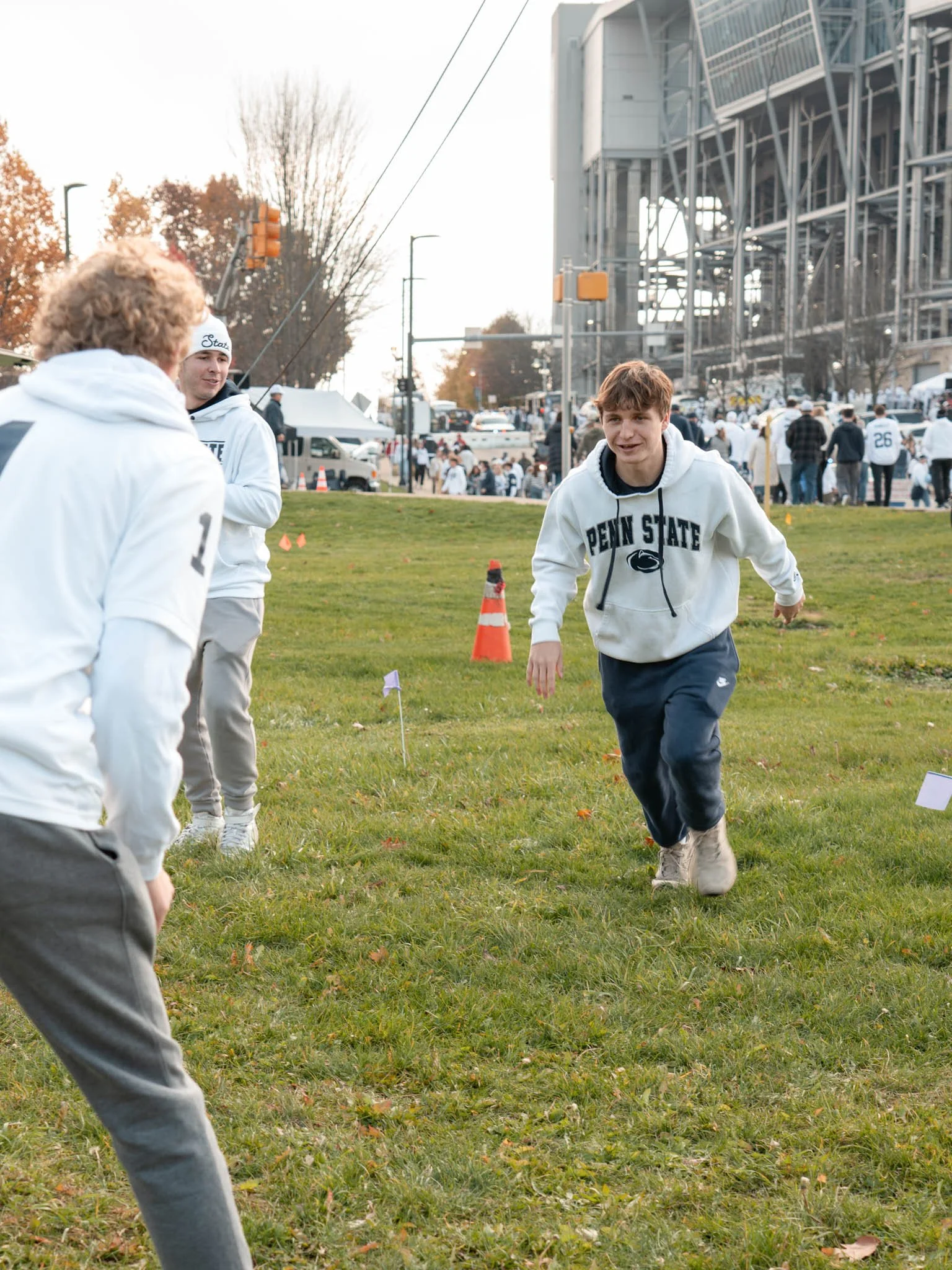 Teenager running in a Penn State hoodie during a college football event on a grassy field.