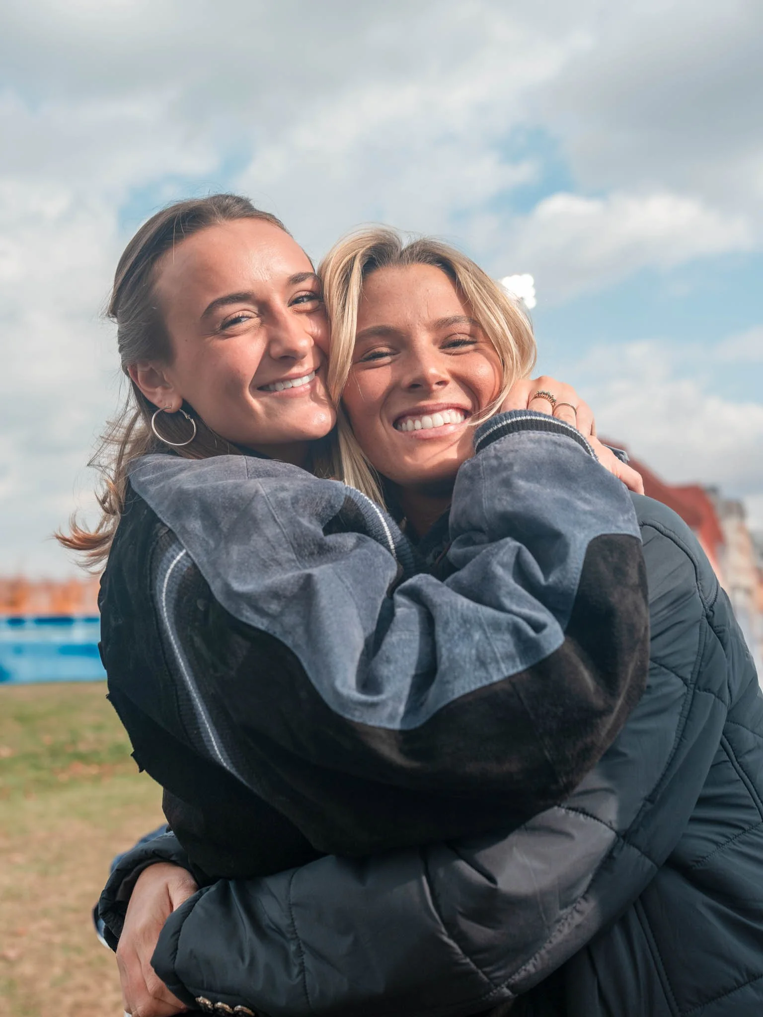 Two smiling women hugging outdoors on a cloudy day.