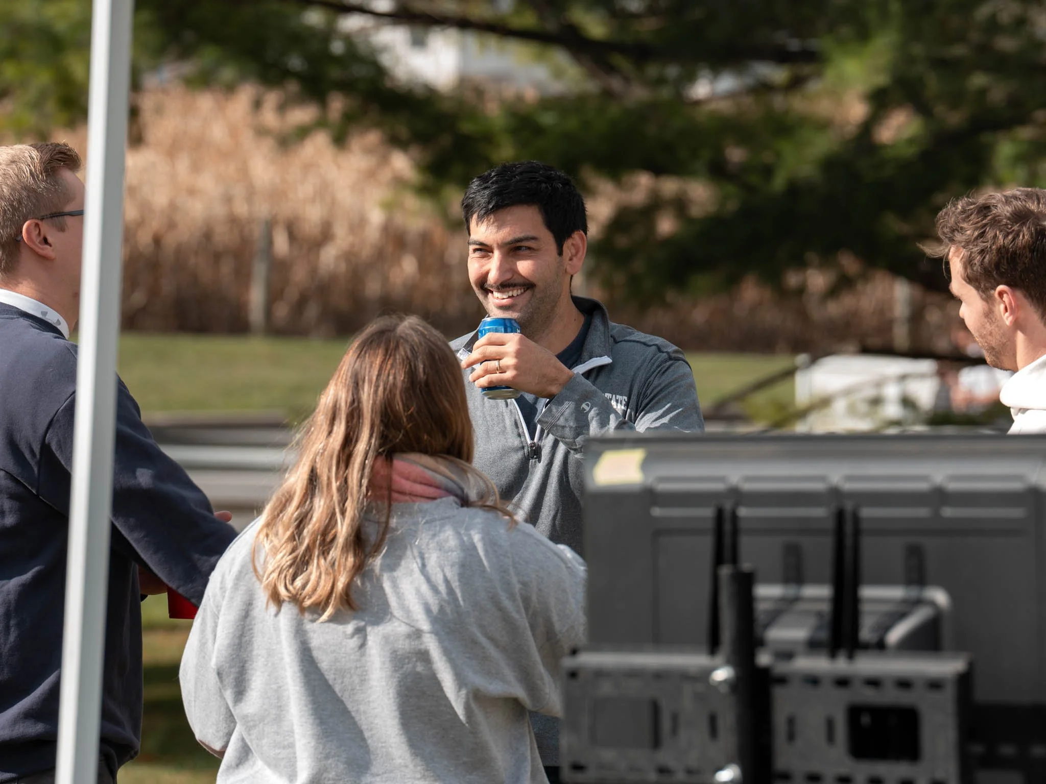 A group of people outdoors enjoying a conversation, with one man smiling and holding a drink.