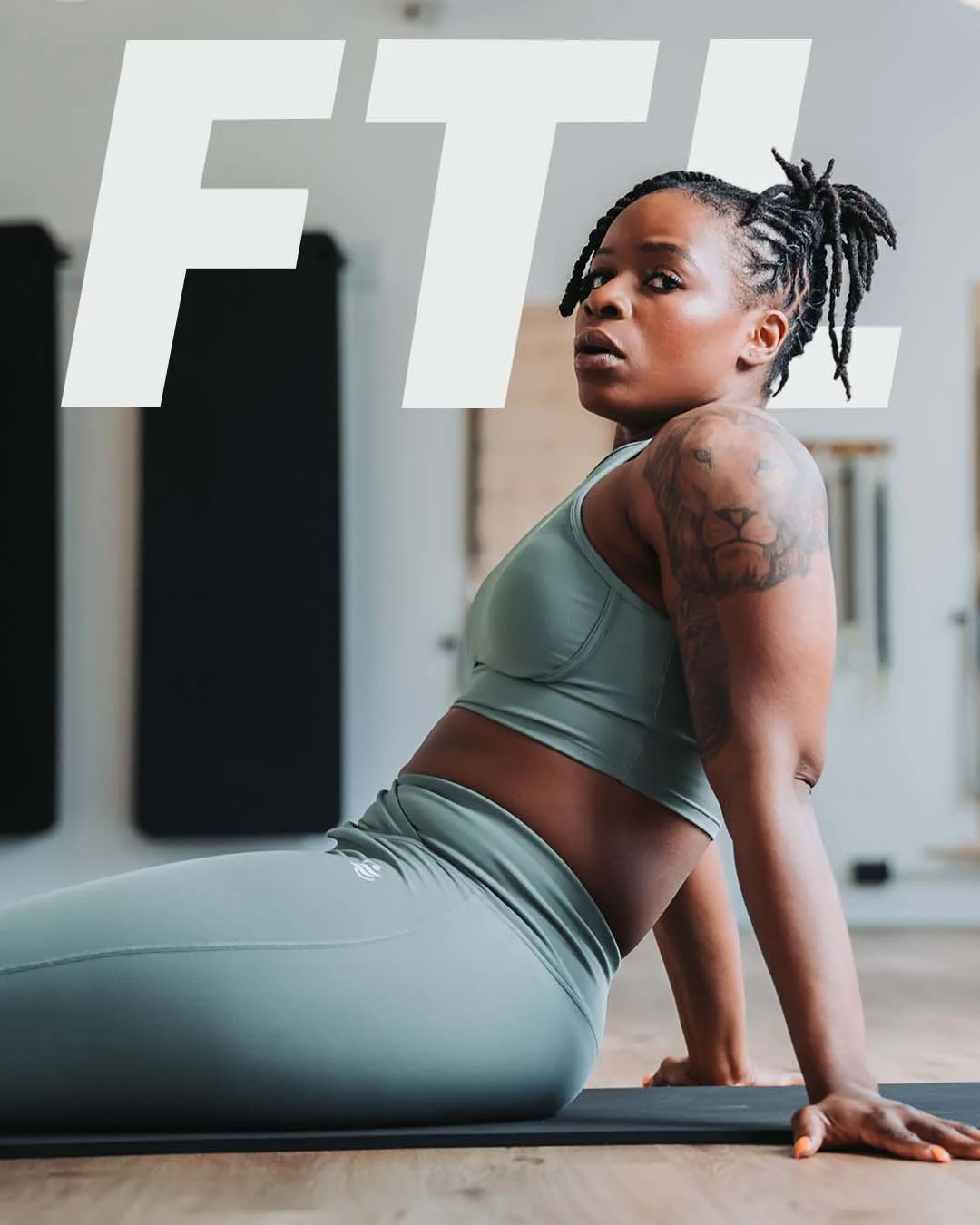 A woman with dreadlocks and tattoos practicing yoga or stretching indoors on a mat with large FTX letters in the background.