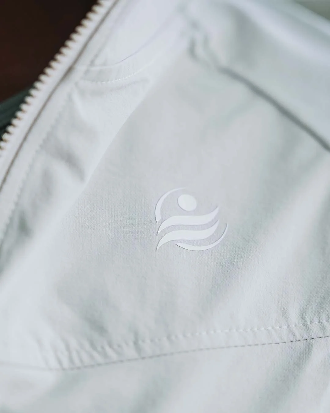 Close-up of a white jacket with a subtle logo featuring a stylized figure and three wavy lines.