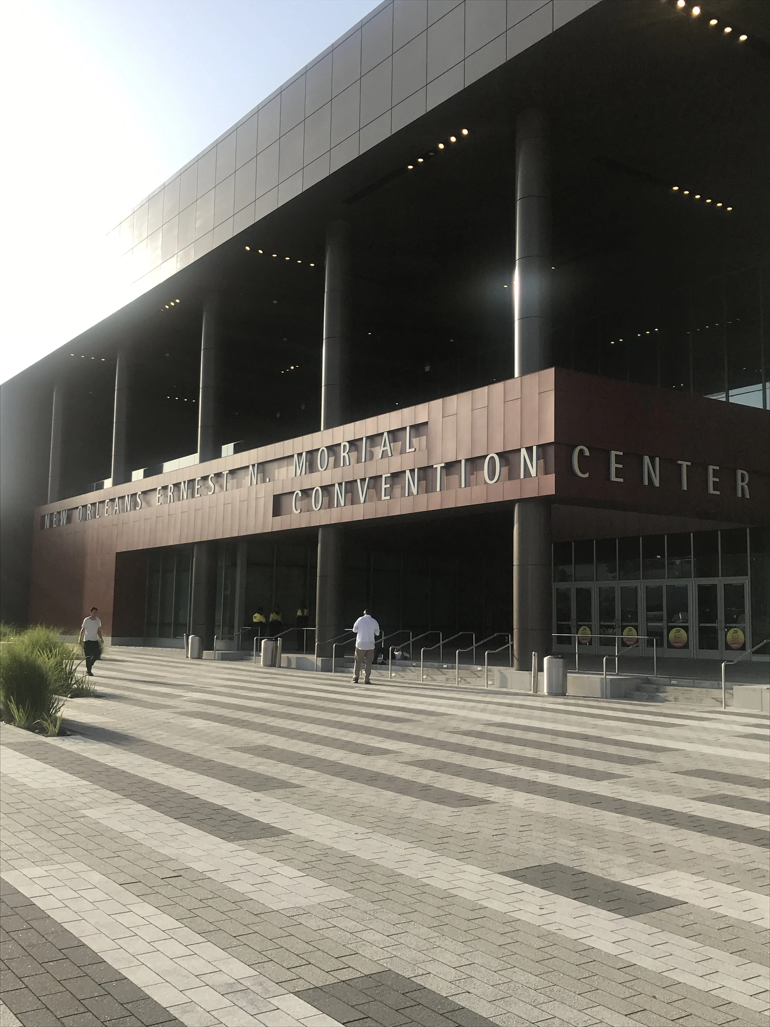 Exterior view of the New Orleans Ernest N. Morial Convention Center, showing the entrance and some pedestrians.