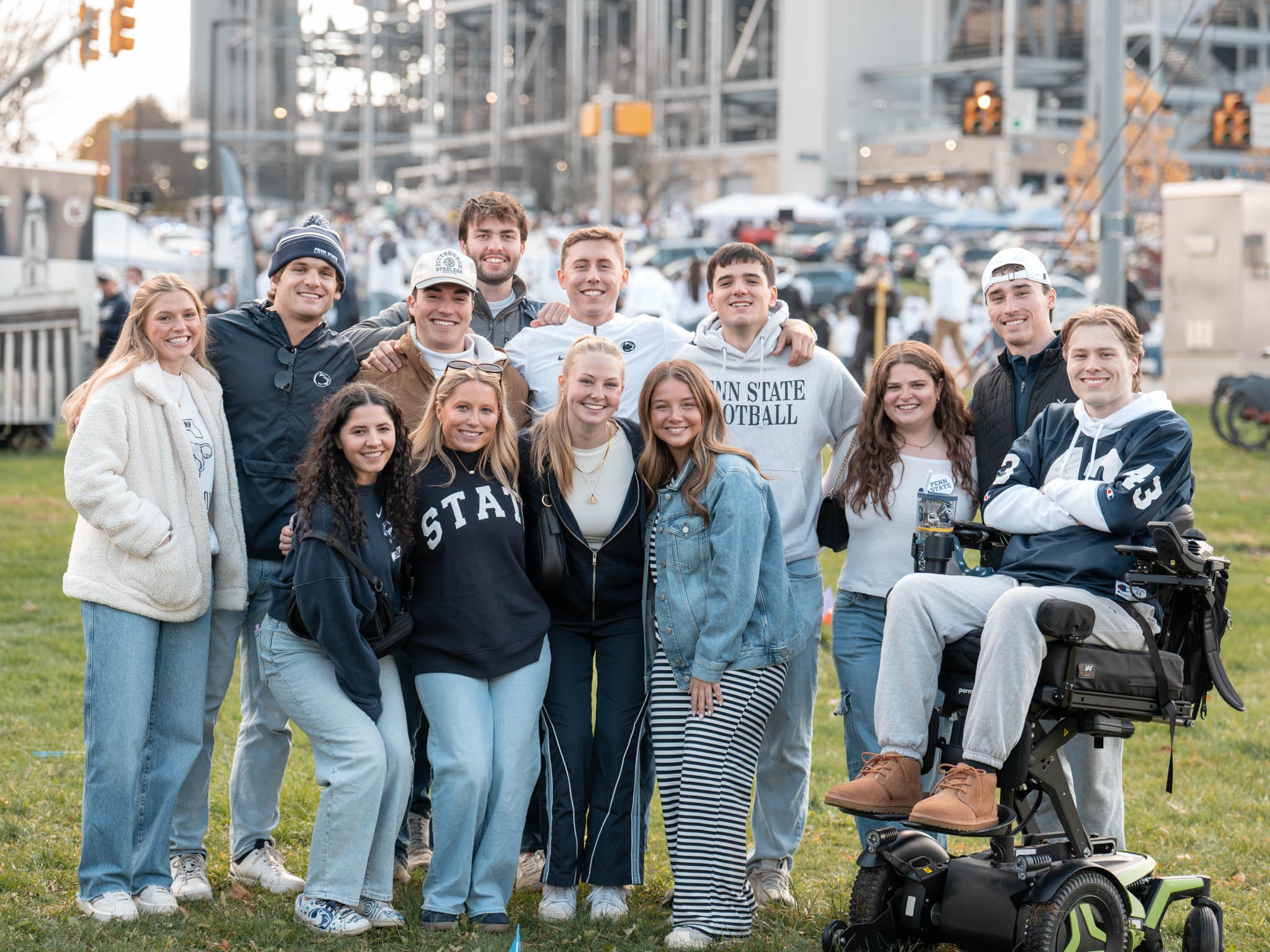 Group of young adults standing outdoors, smiling, with a parking lot and cityscape in the background.