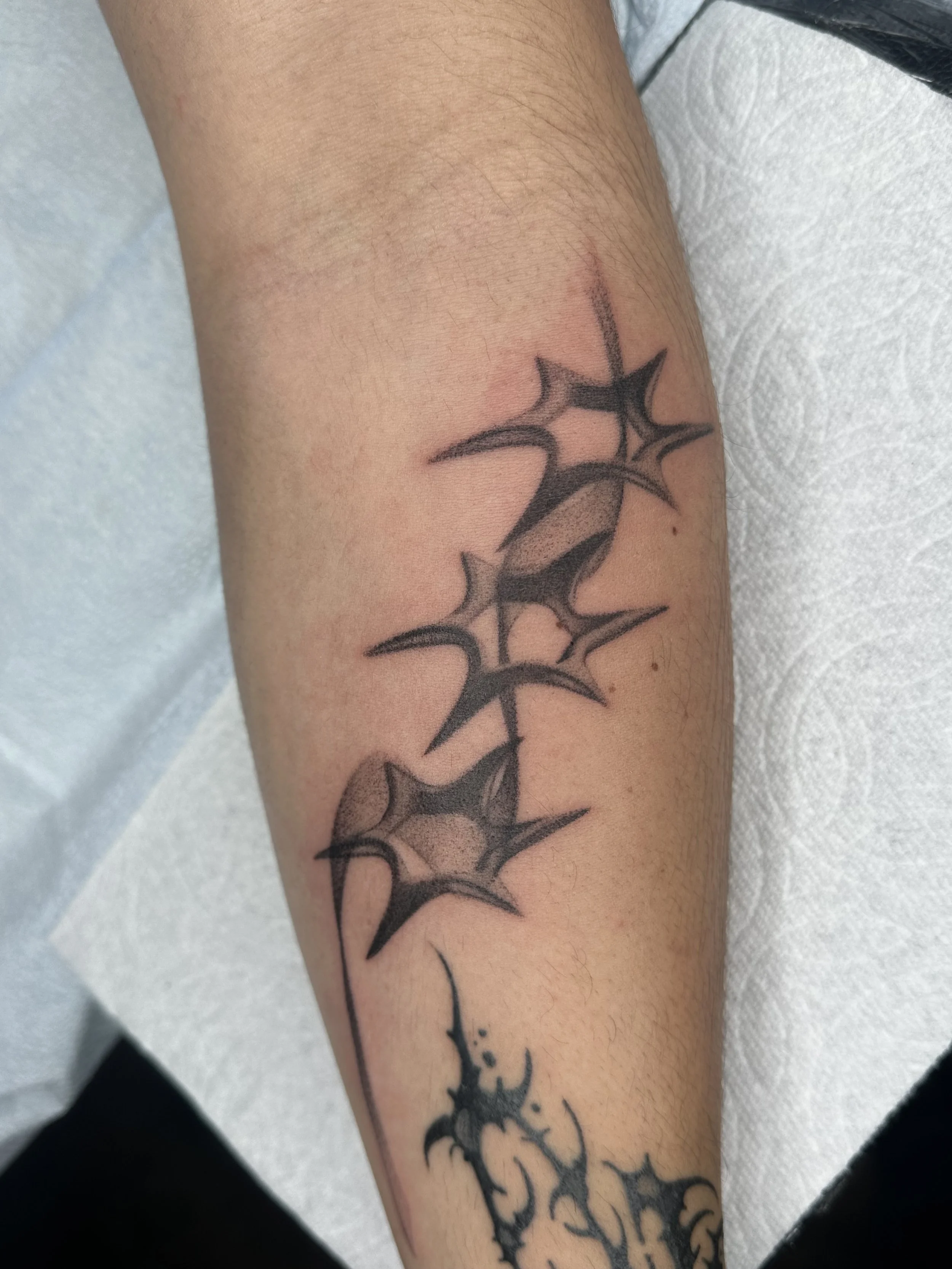Tattoo of three abstract black star-shaped designs along the arm, with a small decorative element underneath.