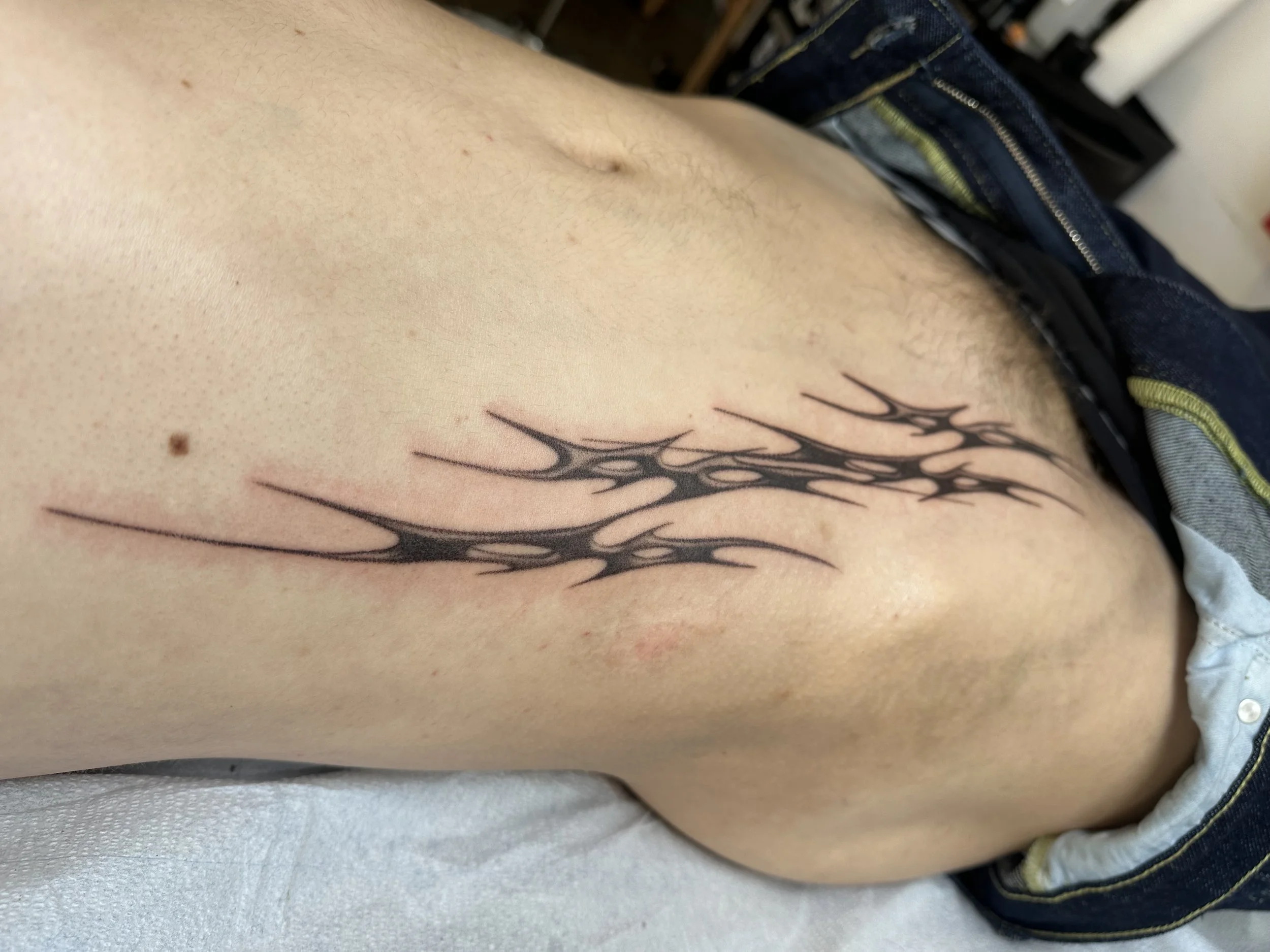 A close-up of a person's side torso showing a tattoo of Neo cybersigilism style flames extending upward.