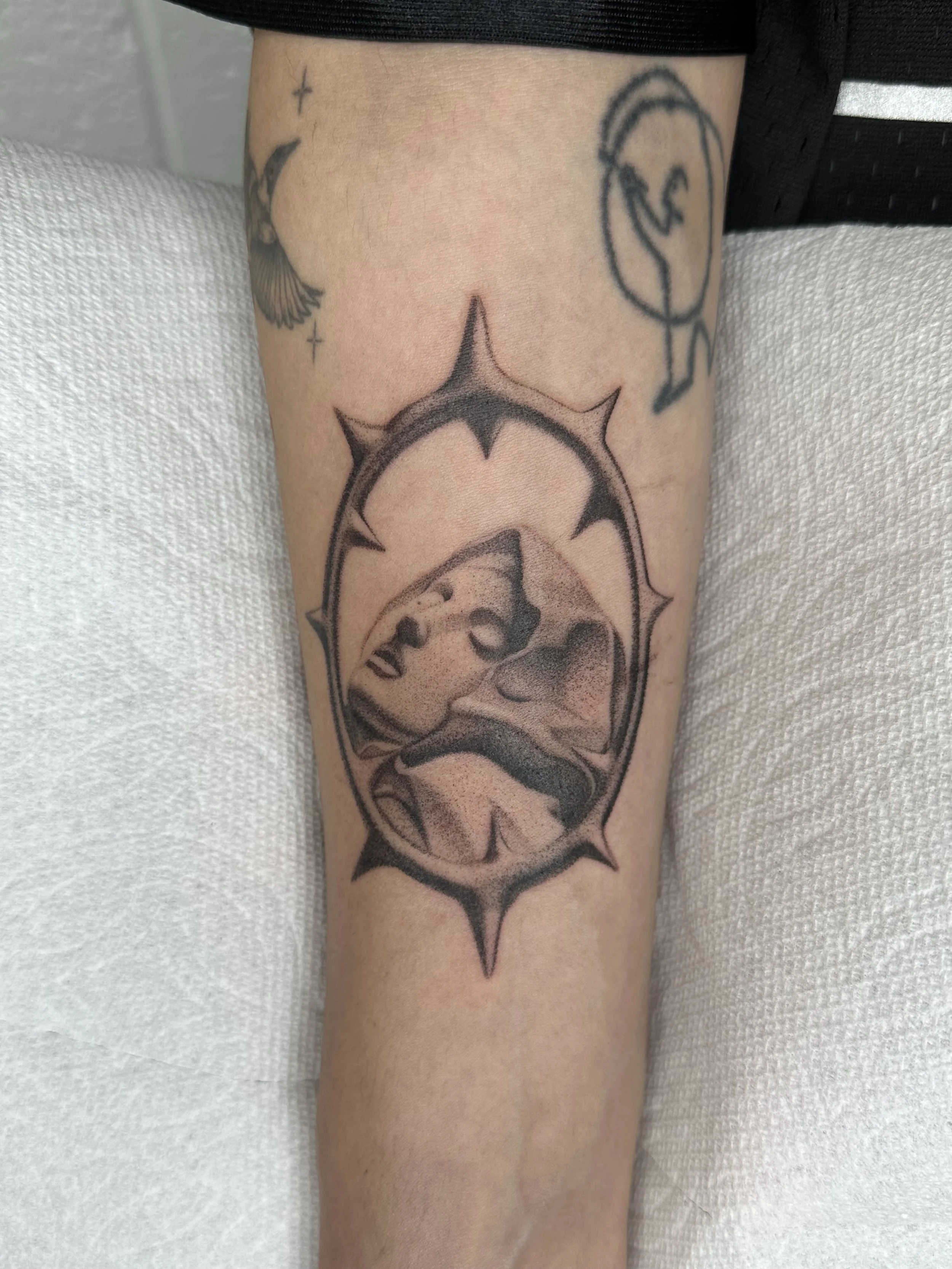 Tattoo of a baroque statue in a circle with a spiked border on a person's forearm.