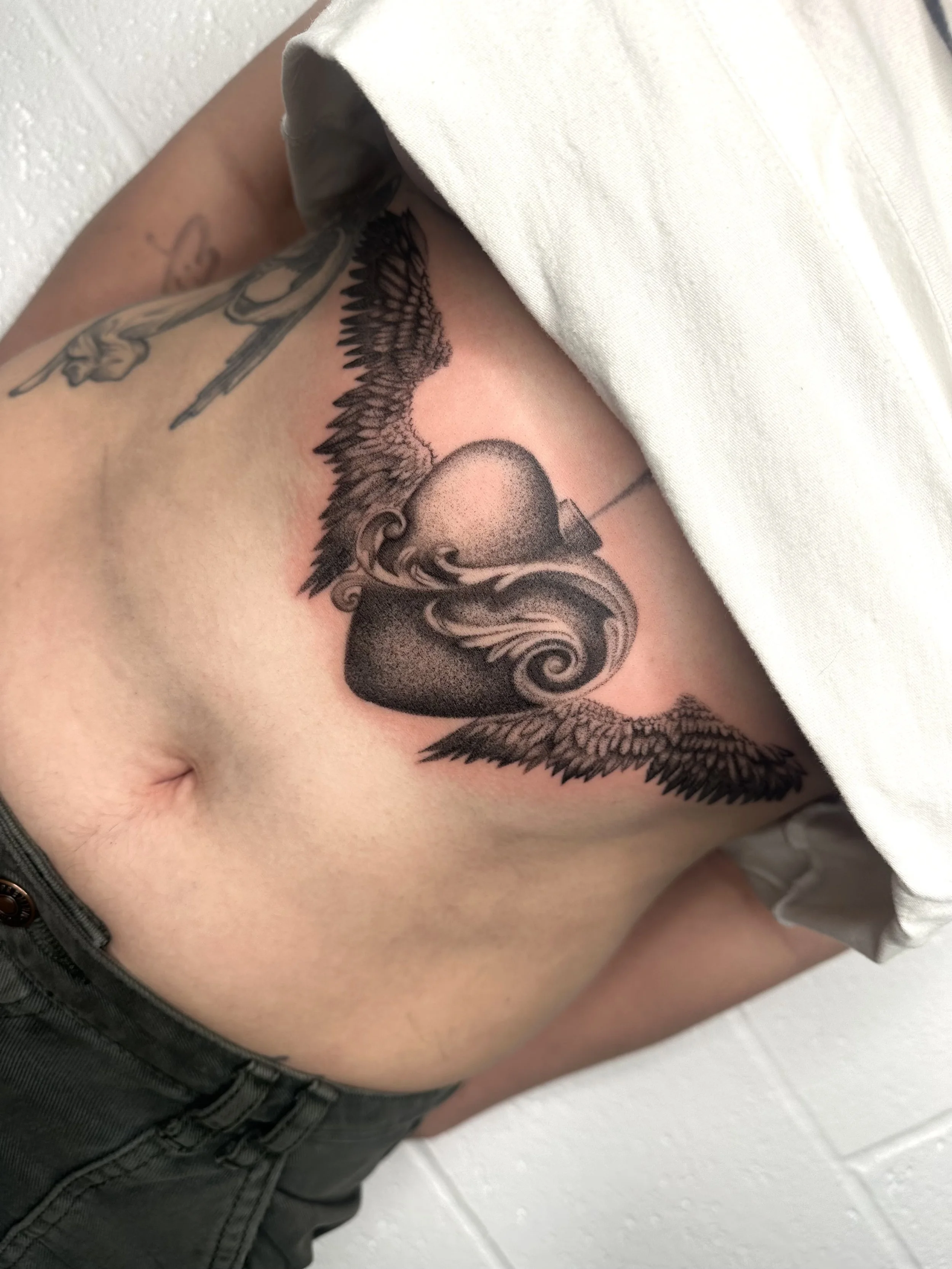 Tattoo of a sacred heart with a filigree on the middle and angel wings on sternum.