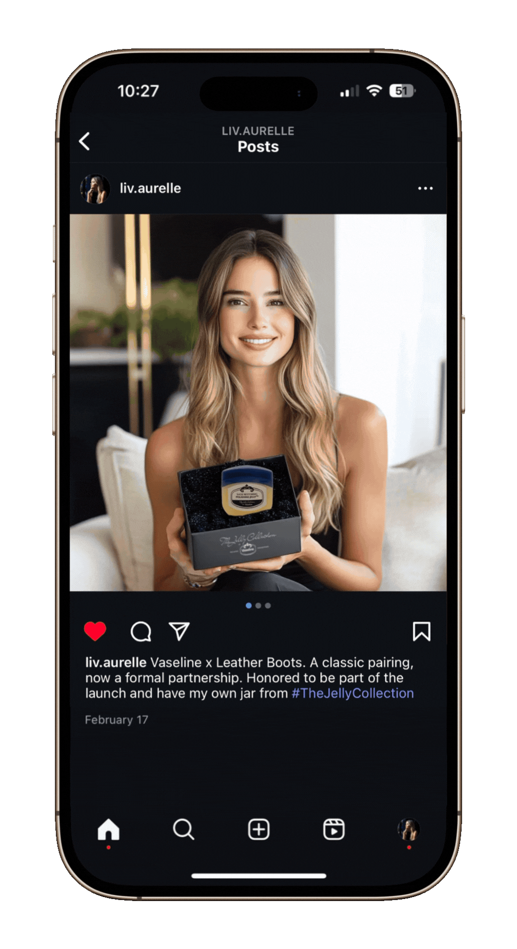 A woman with long, wavy blonde hair smiling and holding a small black box containing a jar of Vaseline x Leather Boots from The Jelly Collection, on a social media post.