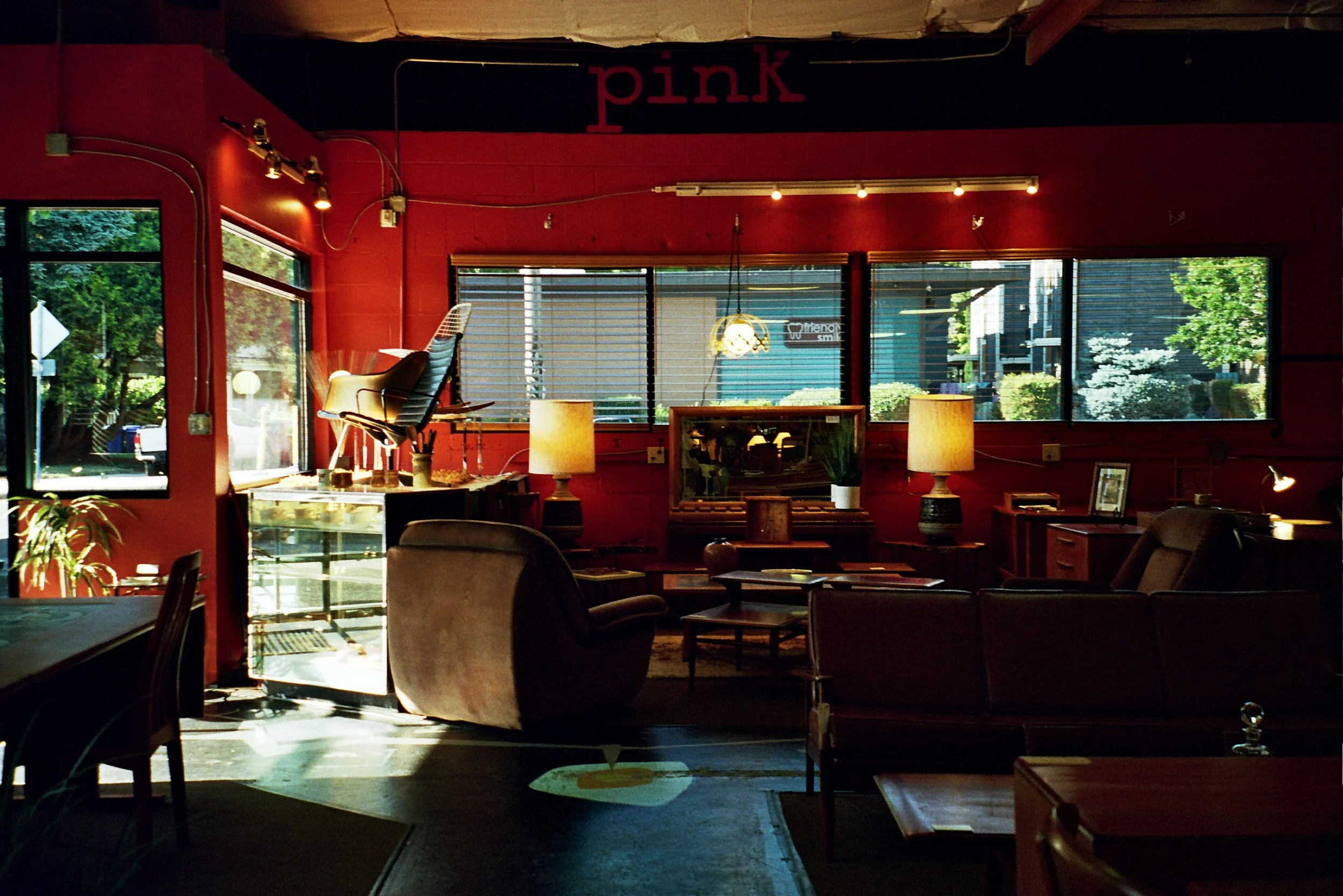 Interior of a cozy cafe with red walls, large windows, and various chairs and tables. There is a sign that says 'pink' on the wall and sunlight streaming through the windows.