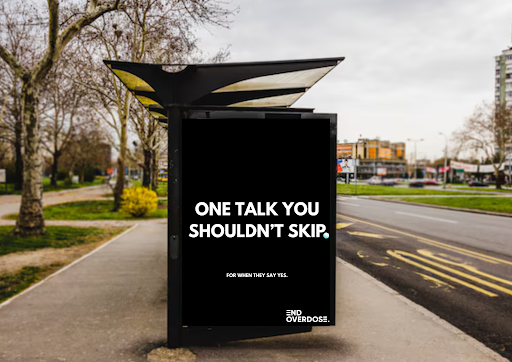 Digital billboard on a sidewalk displaying the message 'ONE TALK YOU SHOULDN'T SKIP FOR WHEN THEY SAY YES. END OVERDOSE!'