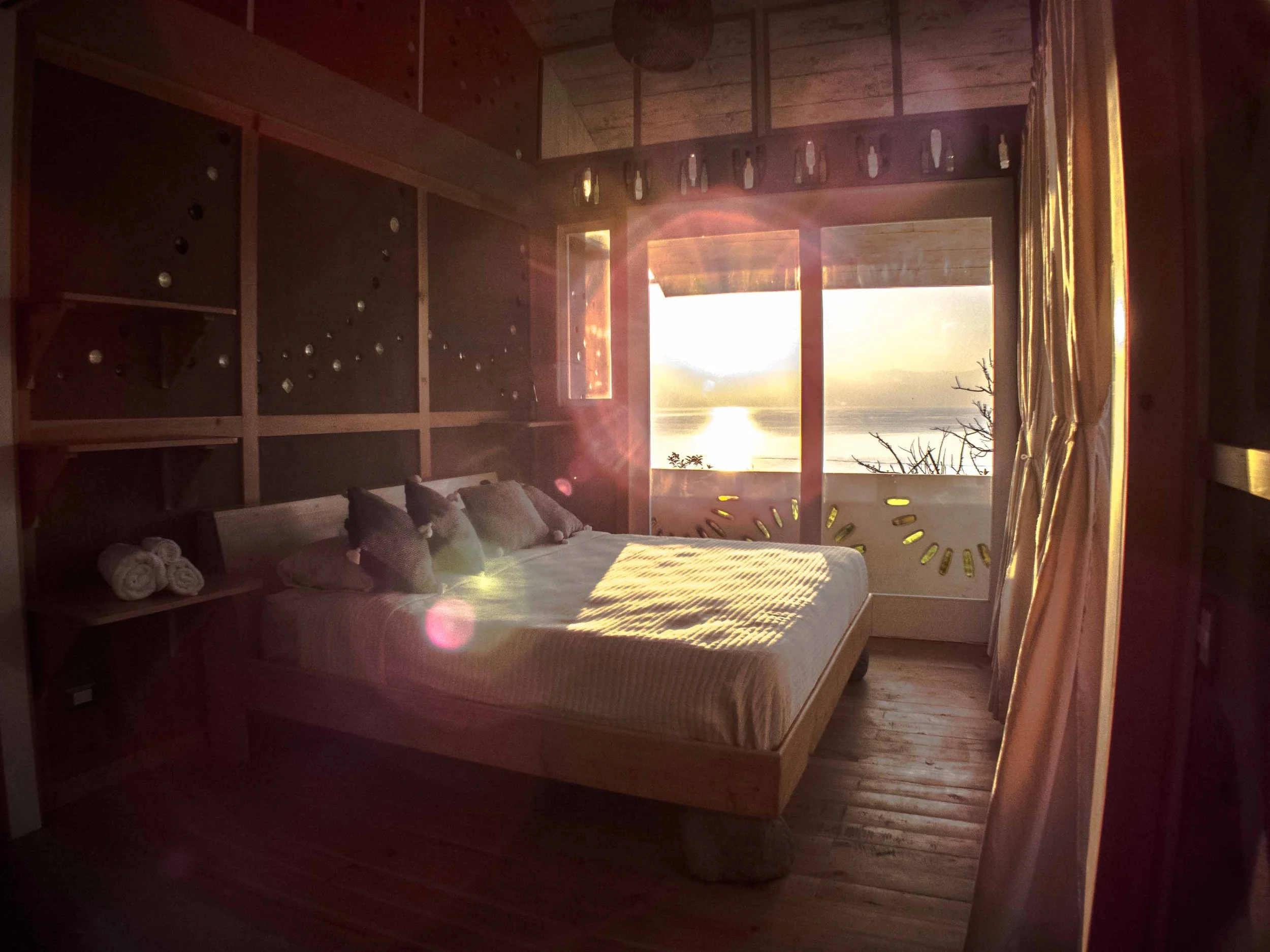 Habitación con cama, ventanas que dejan ver una vista del amanecer o atardecer sobre lago de atitlan, decorada en estilo de madera natural.