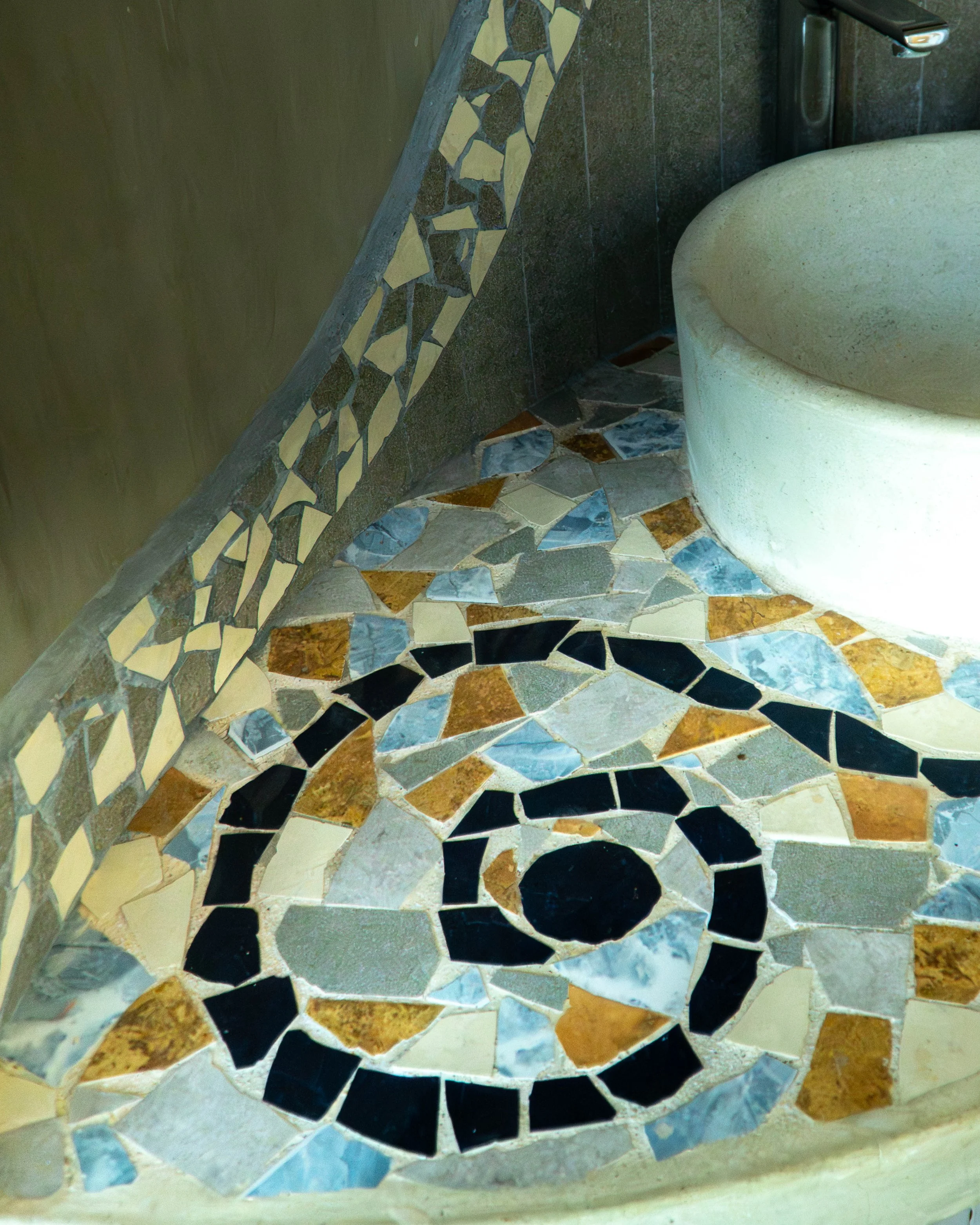 Una esquina de un baño con un inodoro de cerámica de color crema, paredes de color marrón y mosaicos en el suelo y en la parte inferior de la pared con diferentes colores y formas.