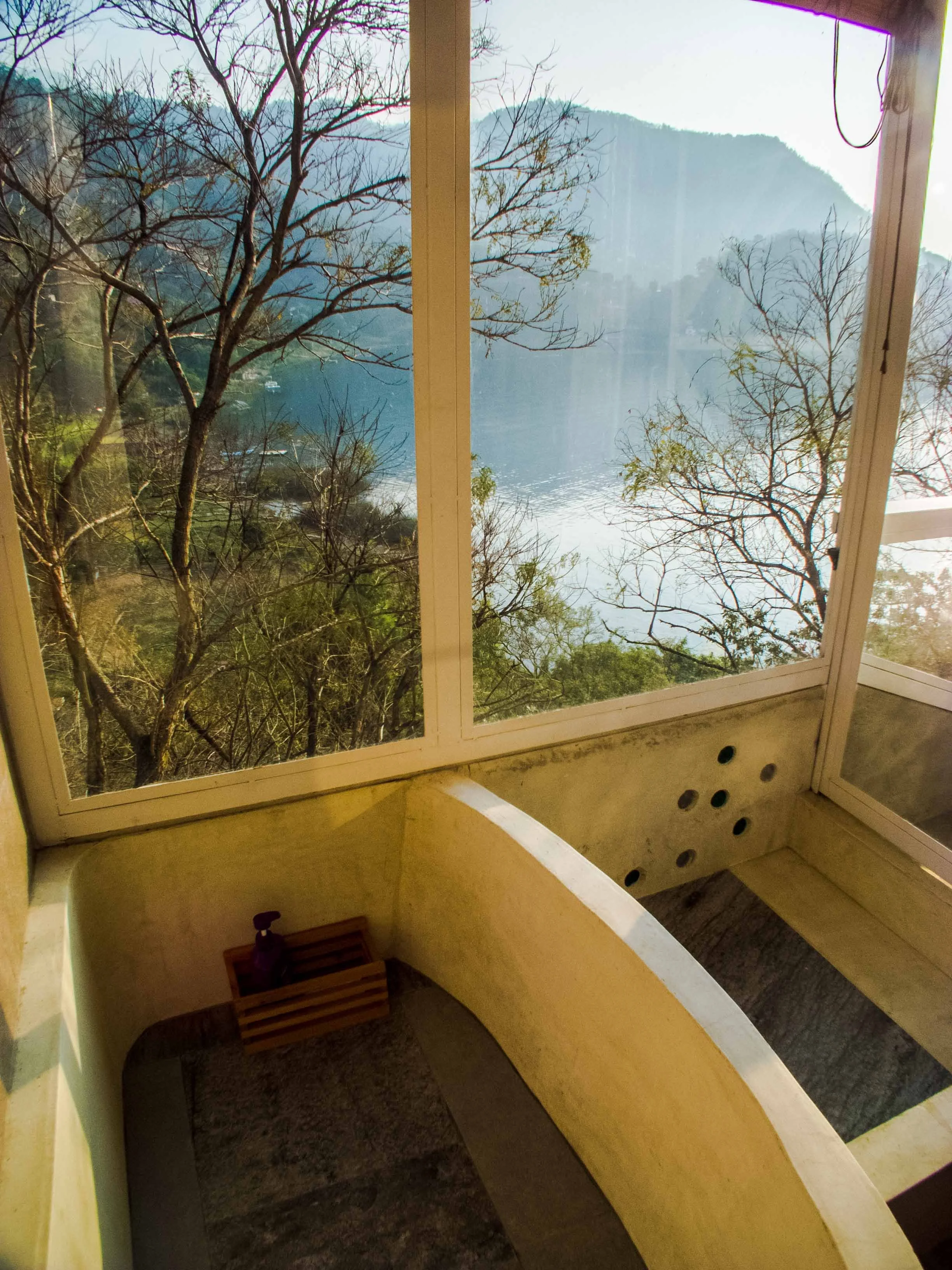Bañera y ducha con vista al Lago y ventana grande mostrando árboles y montañas en un paisaje al aire libre