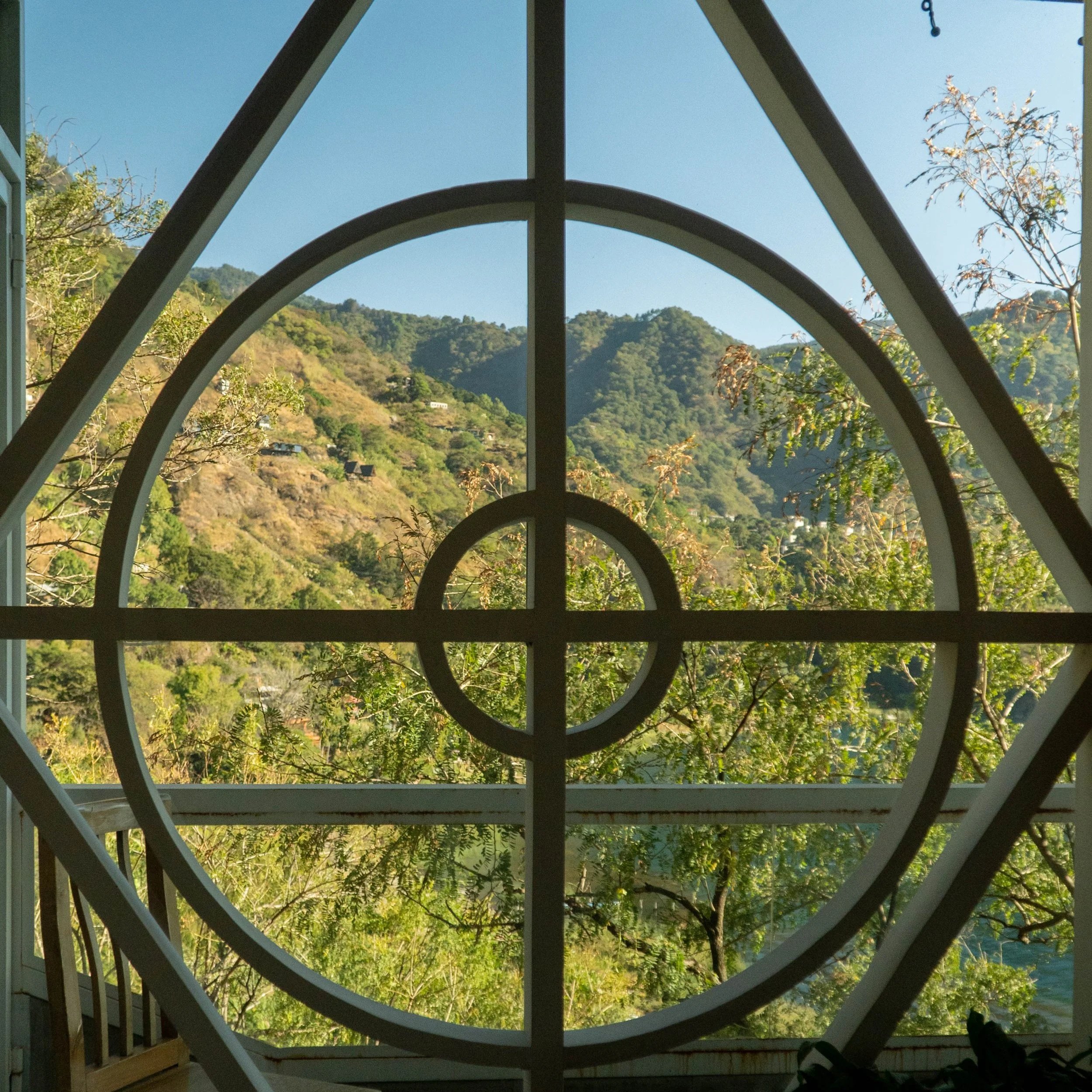 Vista de una montaña con árboles verdes al fondo, vista a través de ventanas con rejas decorativas en forma de círculos