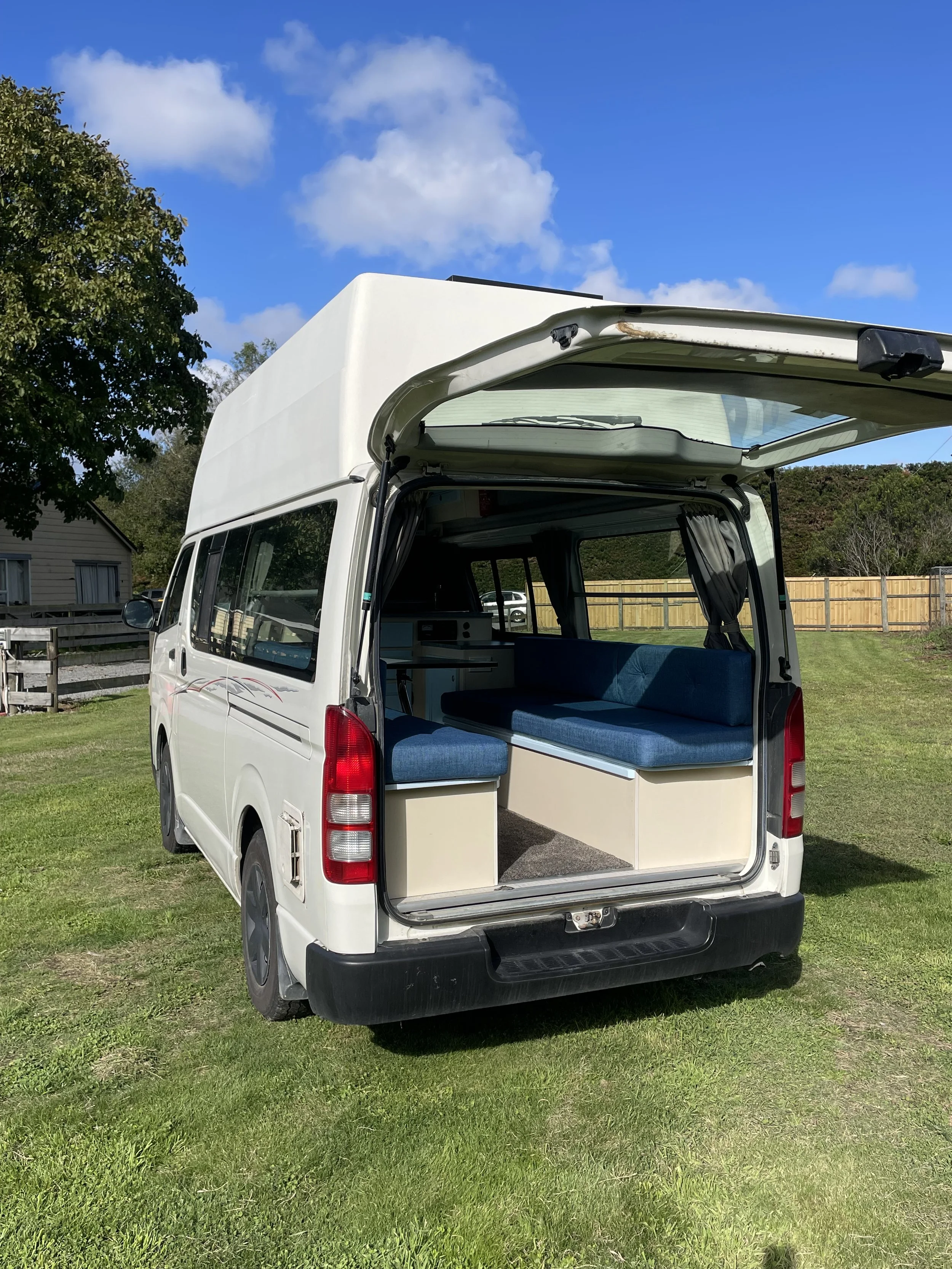 Under a desk, there are charging devices and cables plugged into an electrical outlet, with a blue chair nearby and some equipment on the floor.