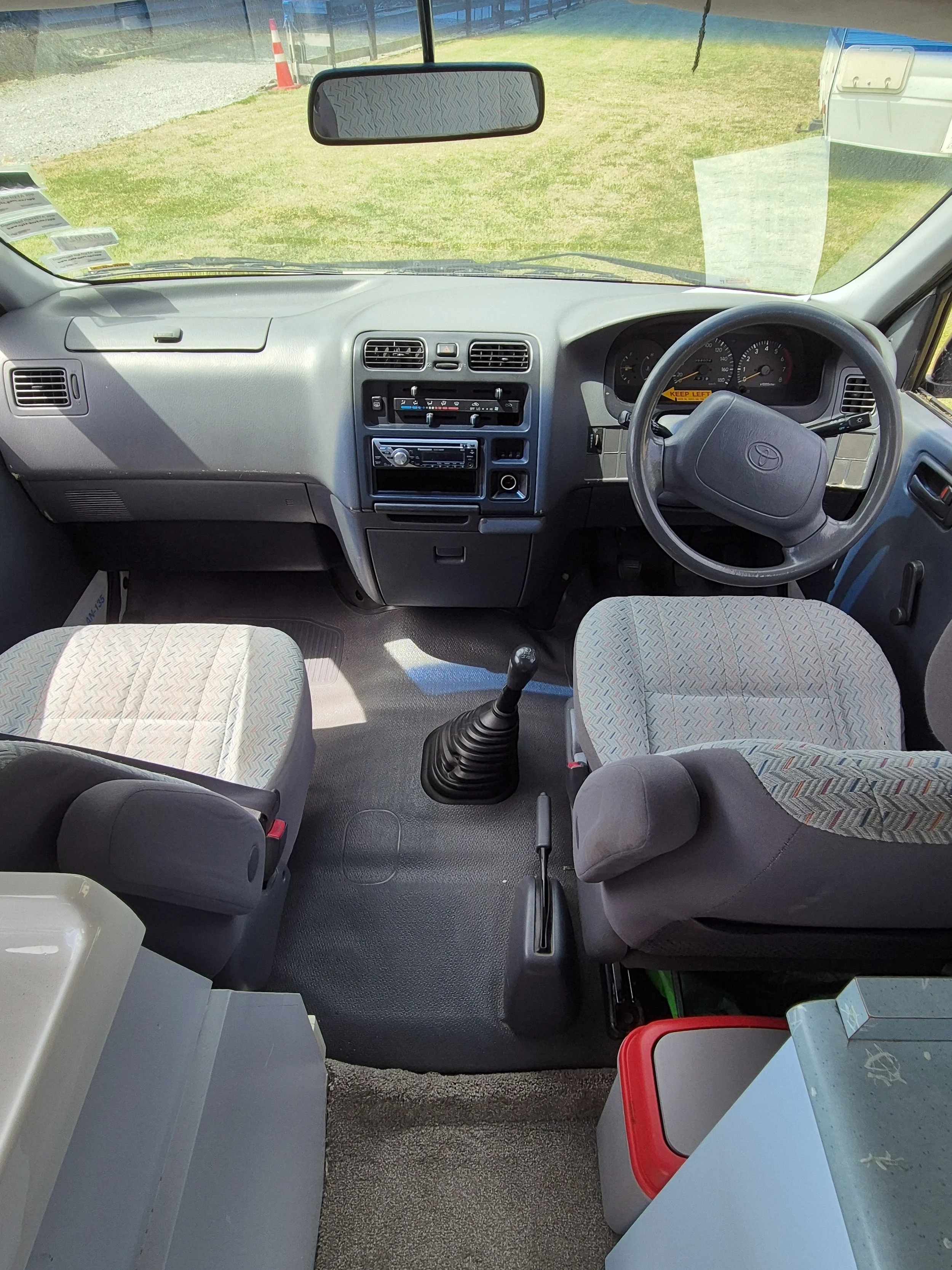Under a desk, there are charging devices and cables plugged into an electrical outlet, with a blue chair nearby and some equipment on the floor.
