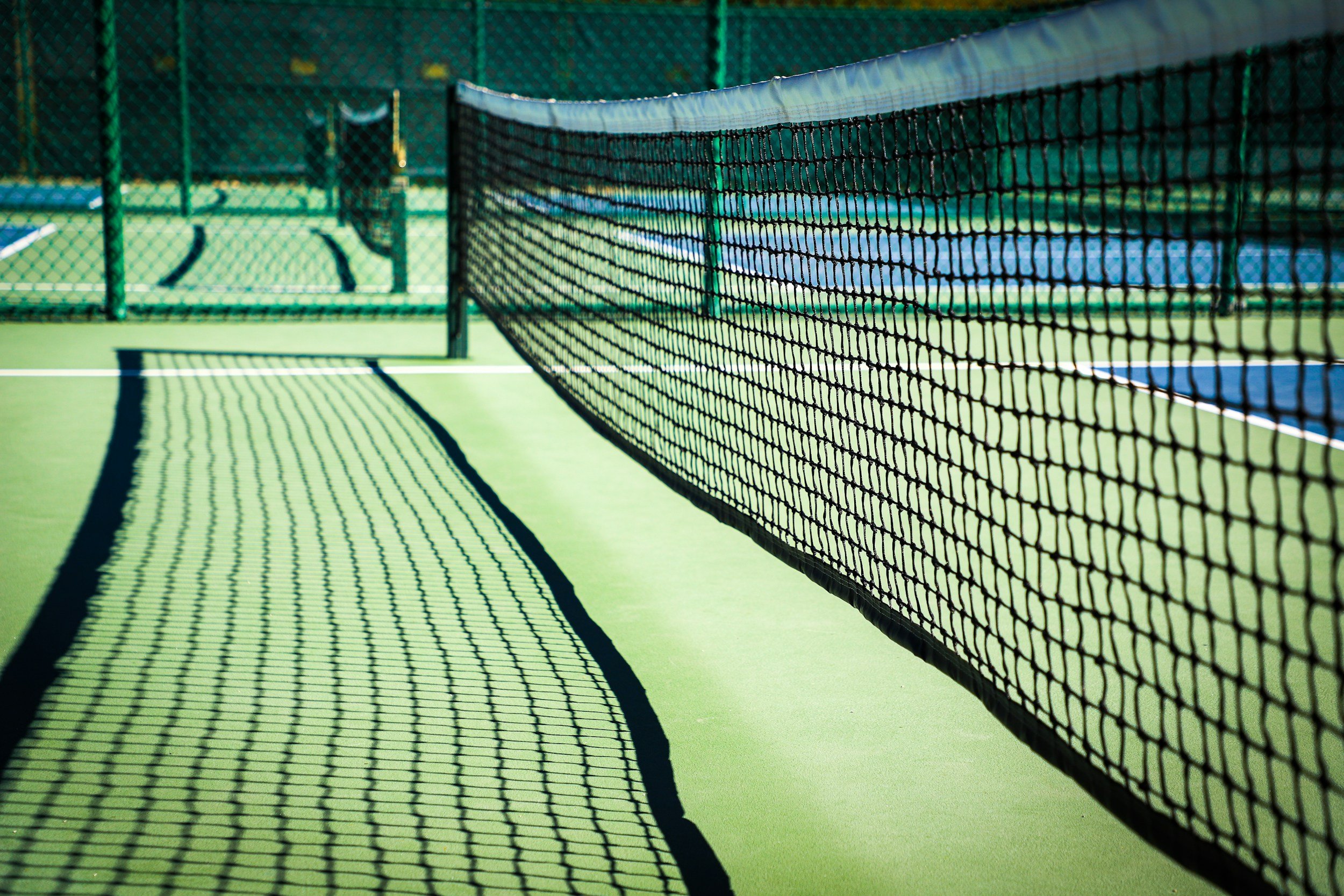 Empty tennis court with green surface, black net, and surrounding green fences.