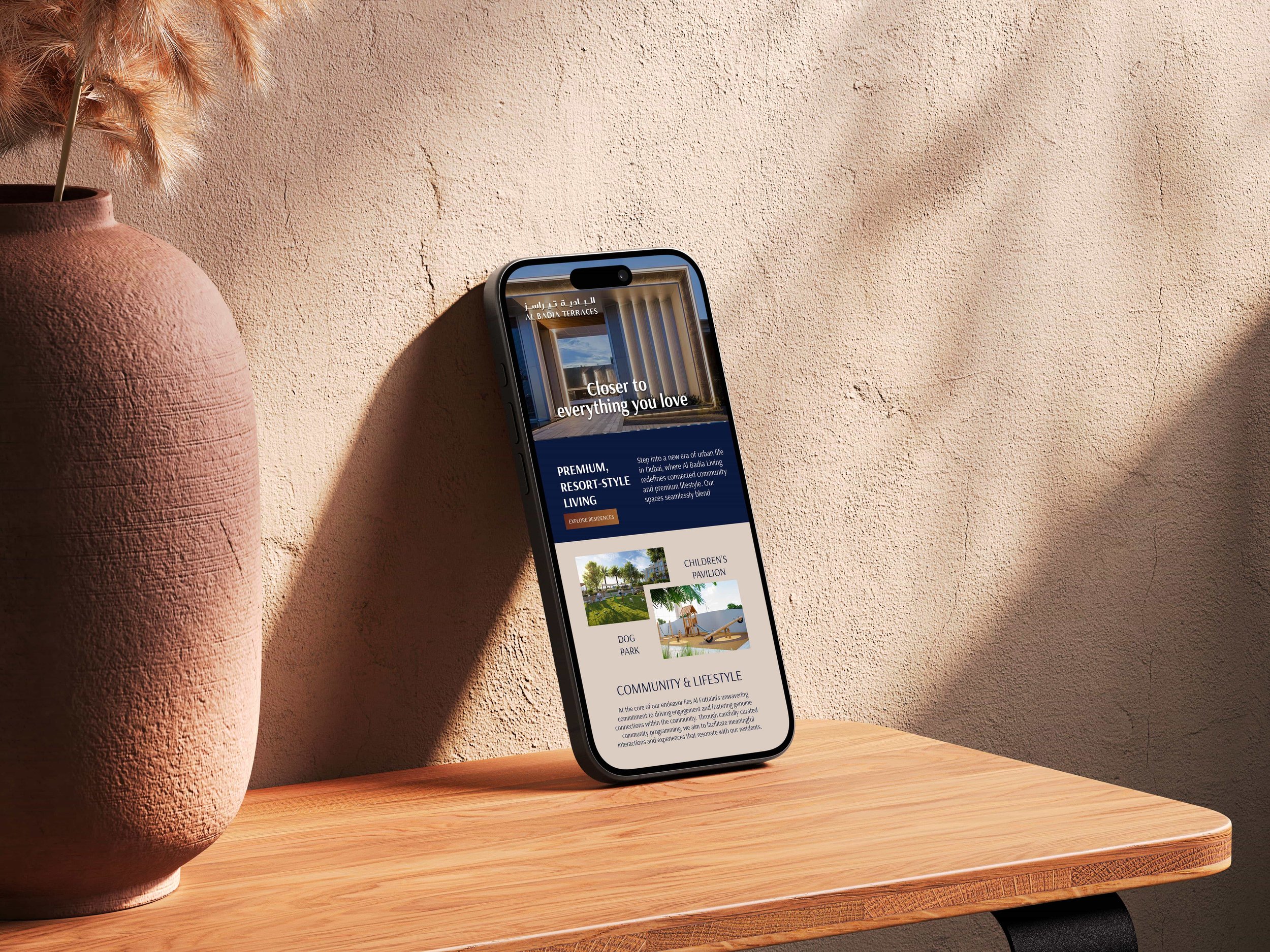 Destination Branding. Smartphone displaying a website on a wooden table next to a large clay vase with dried ornamental grass. The background is a textured beige wall with shadows.