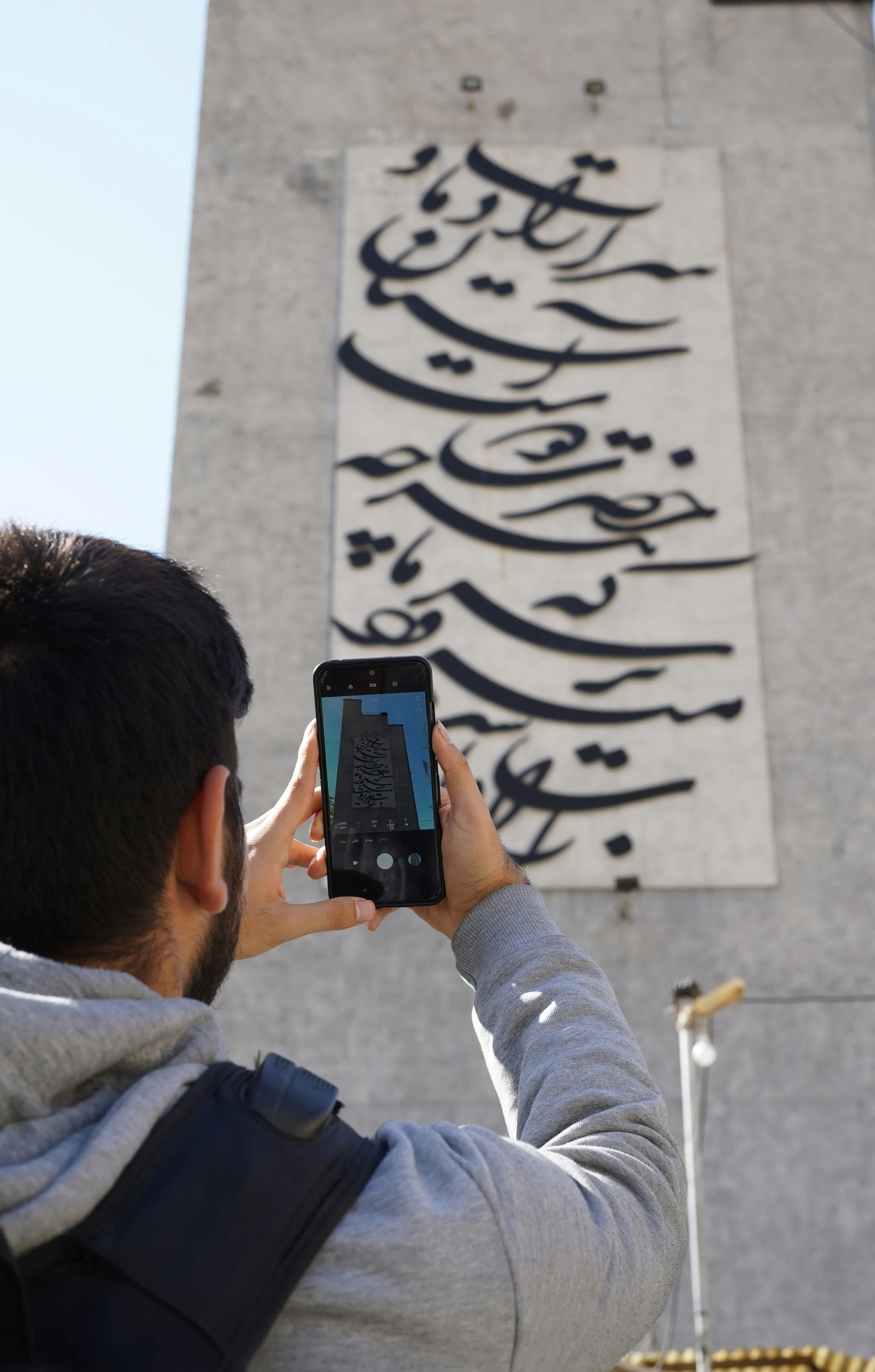 Placemaking. A man taking a photo of a large wall-mounted Arabic calligraphic artwork with his smartphone.