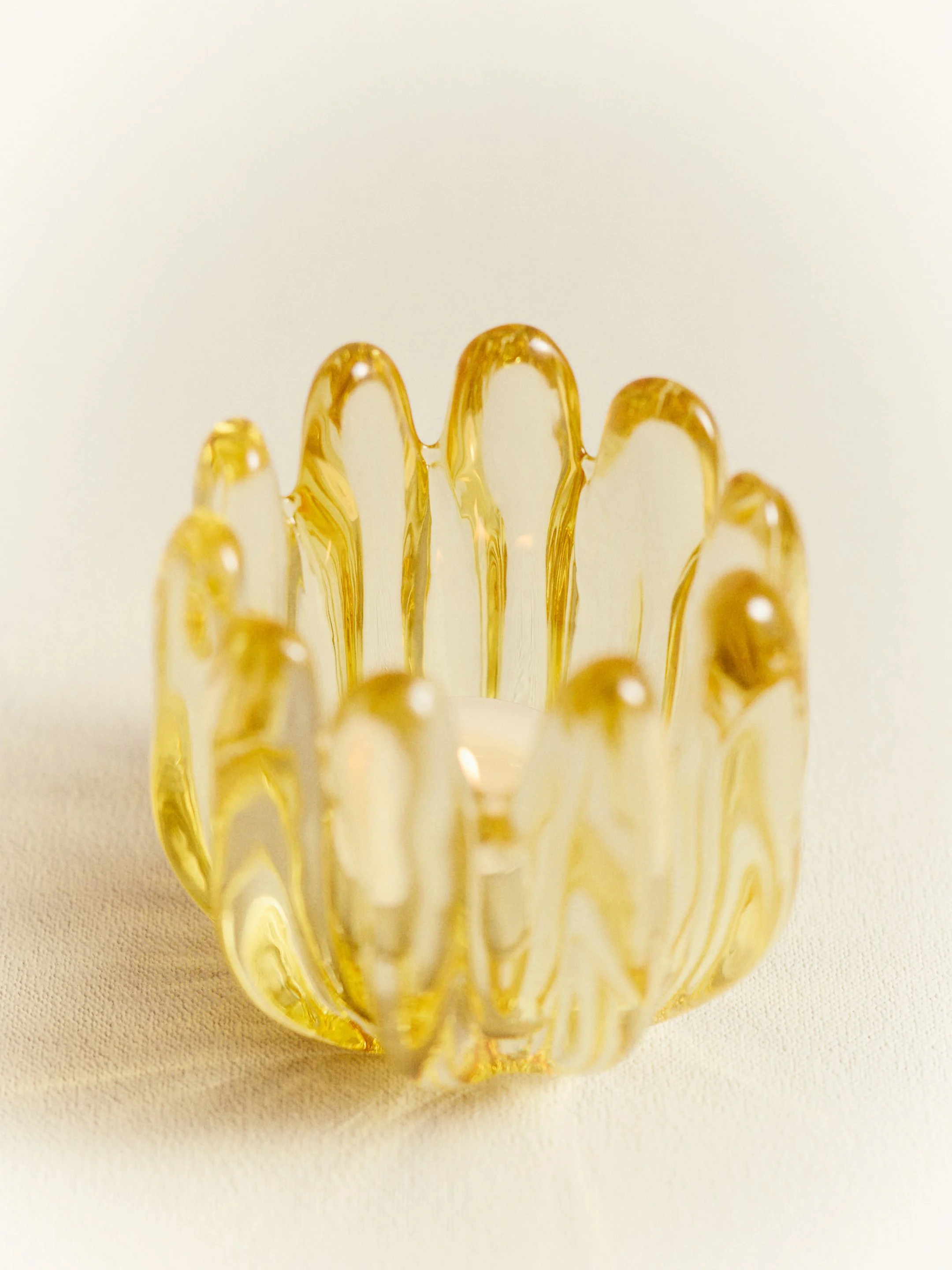 A decorative glass candle holder with a marbled yellow and white pattern, holding a lit white candle inside.