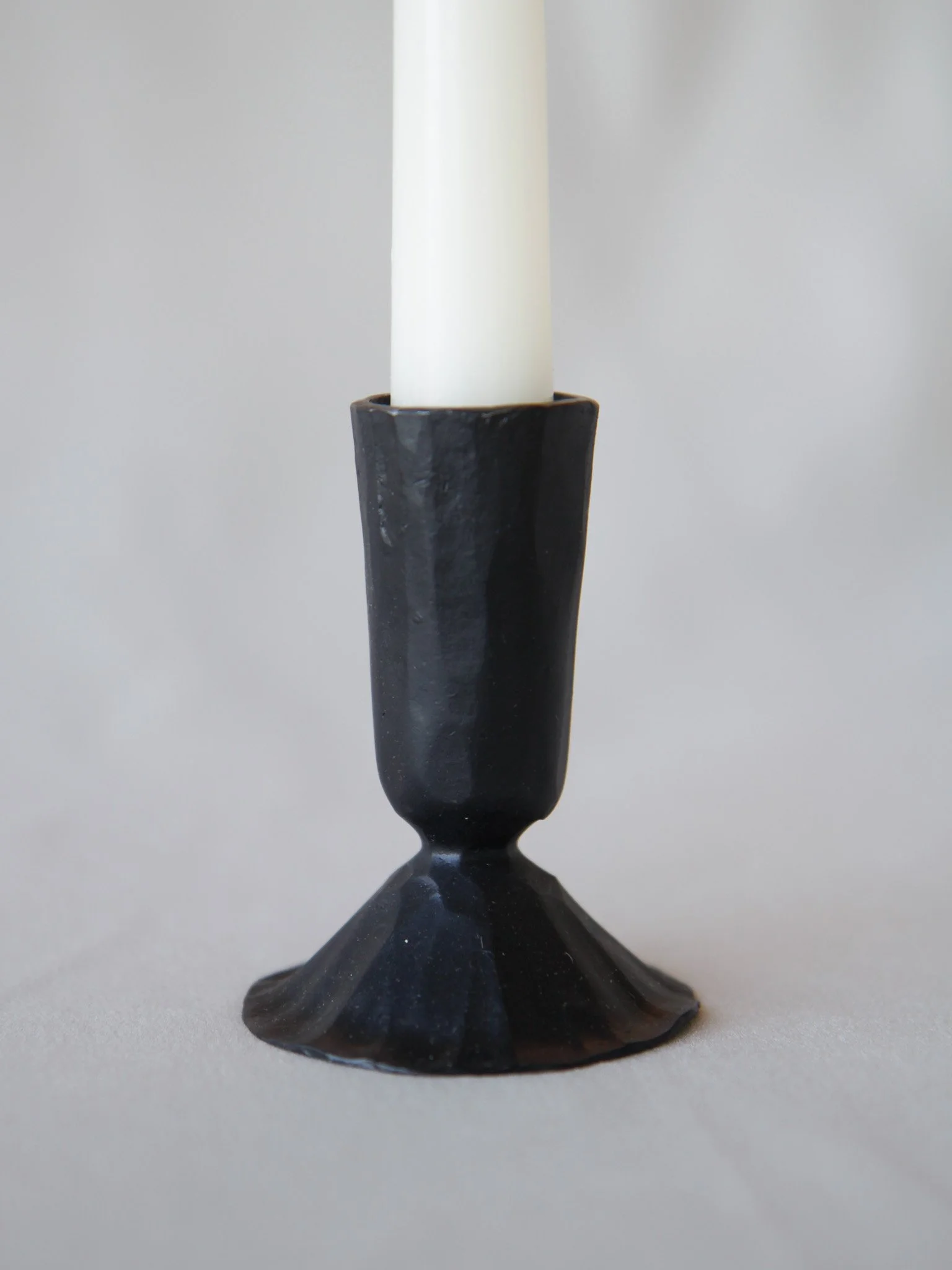 Black ceramic candlestick holder with a white candle on a light surface.
