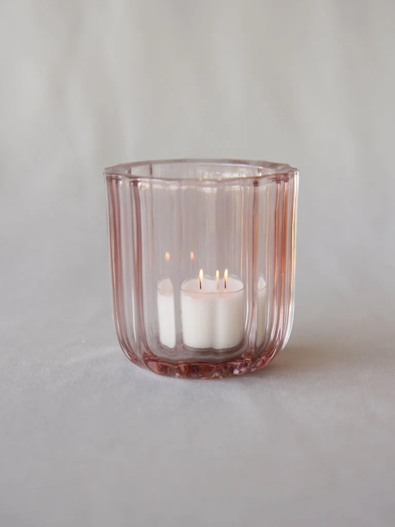 Pink glass candle holder with a white candle inside and three small flames