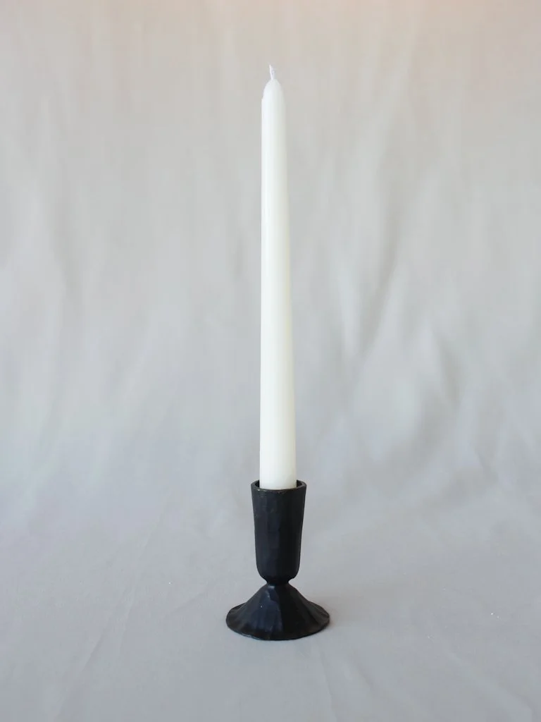 White candle in a black candle holder on a light background.