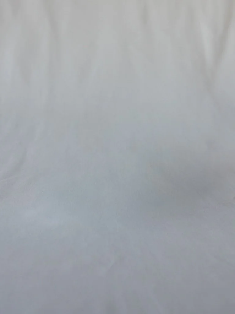 A blank surface, possibly paper or fabric, with a smooth, light-colored texture.