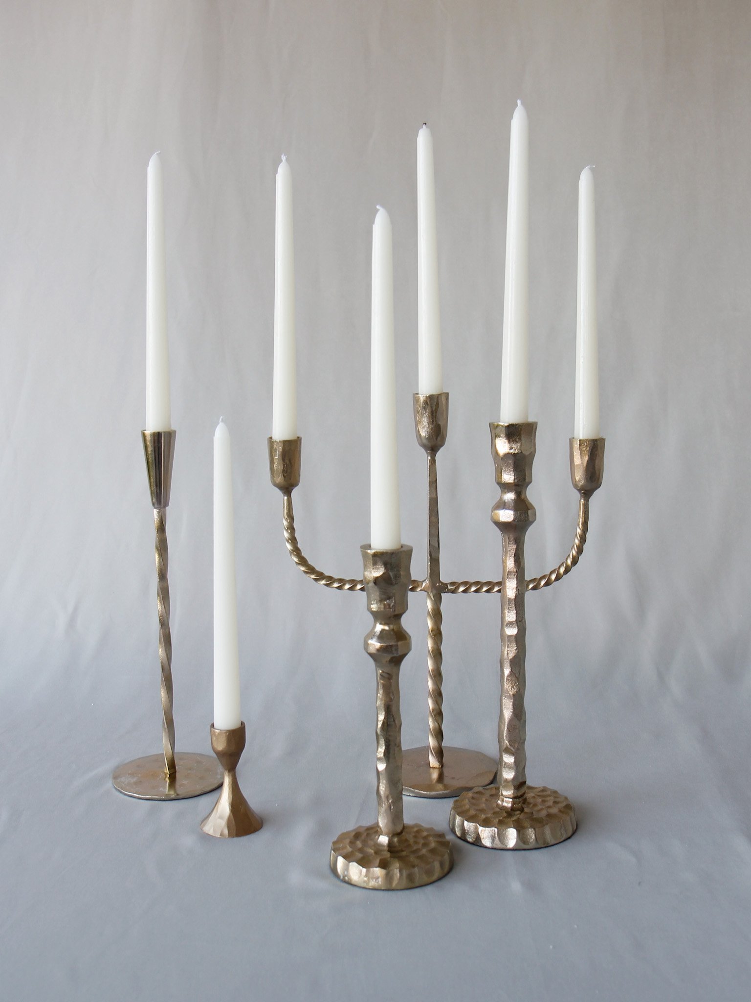 Brass menorah with nine white candles, some lit, on a light gray background.