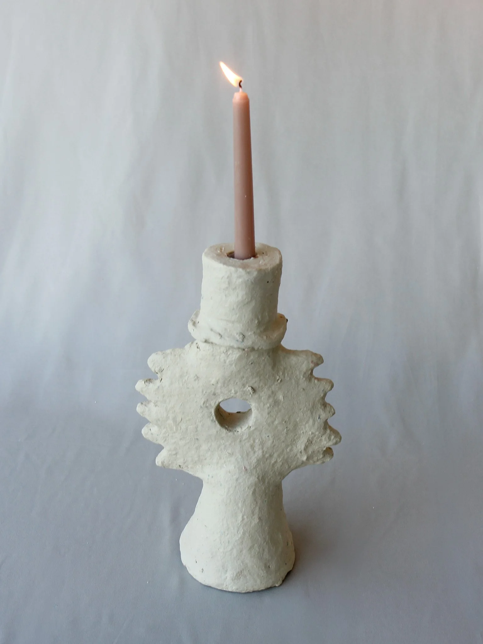 Candle holder shaped like a human figure with a spiky circular shape around the head, holding a lit candle.