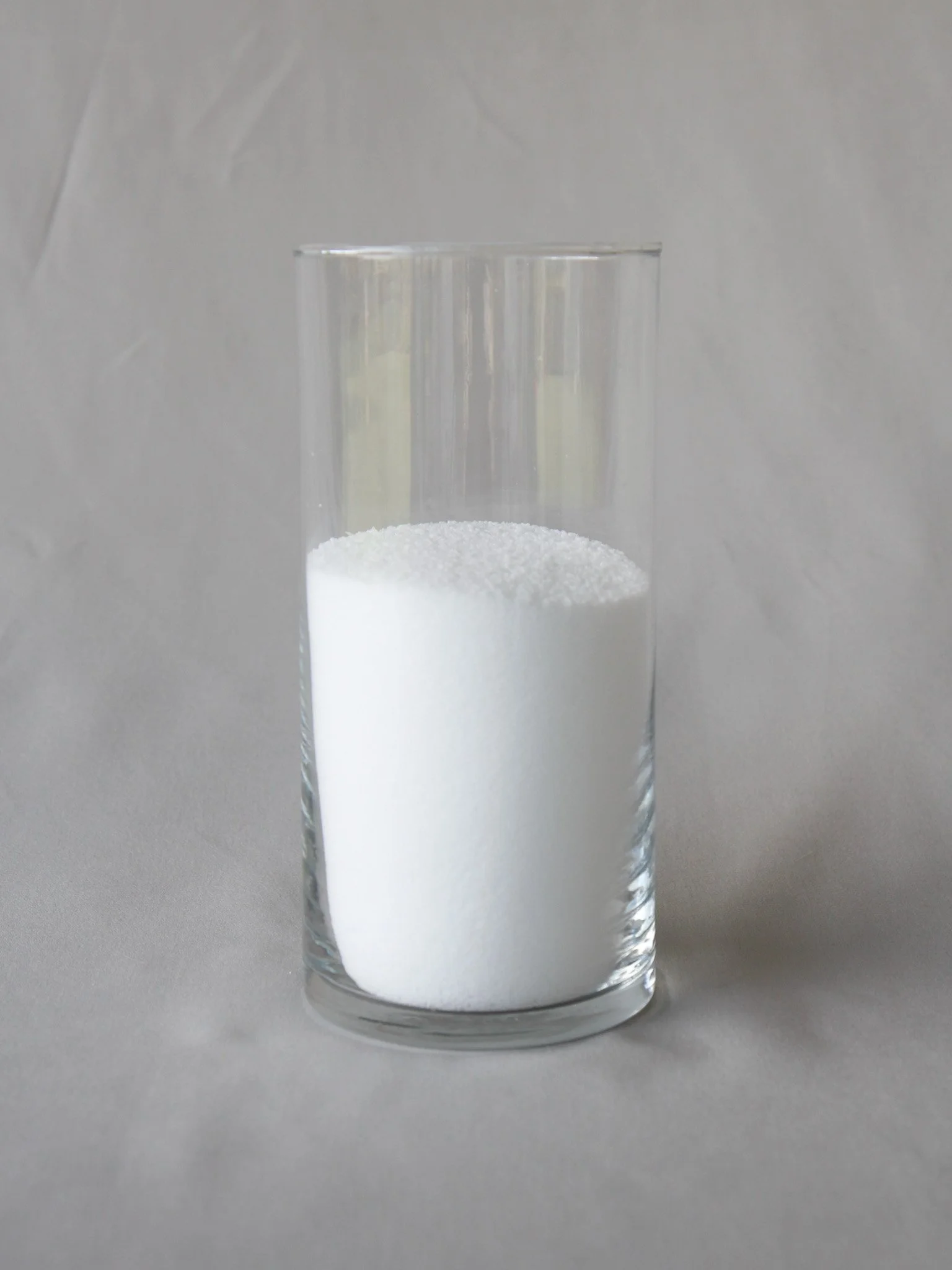 Glass of white granular salt on a gray surface.