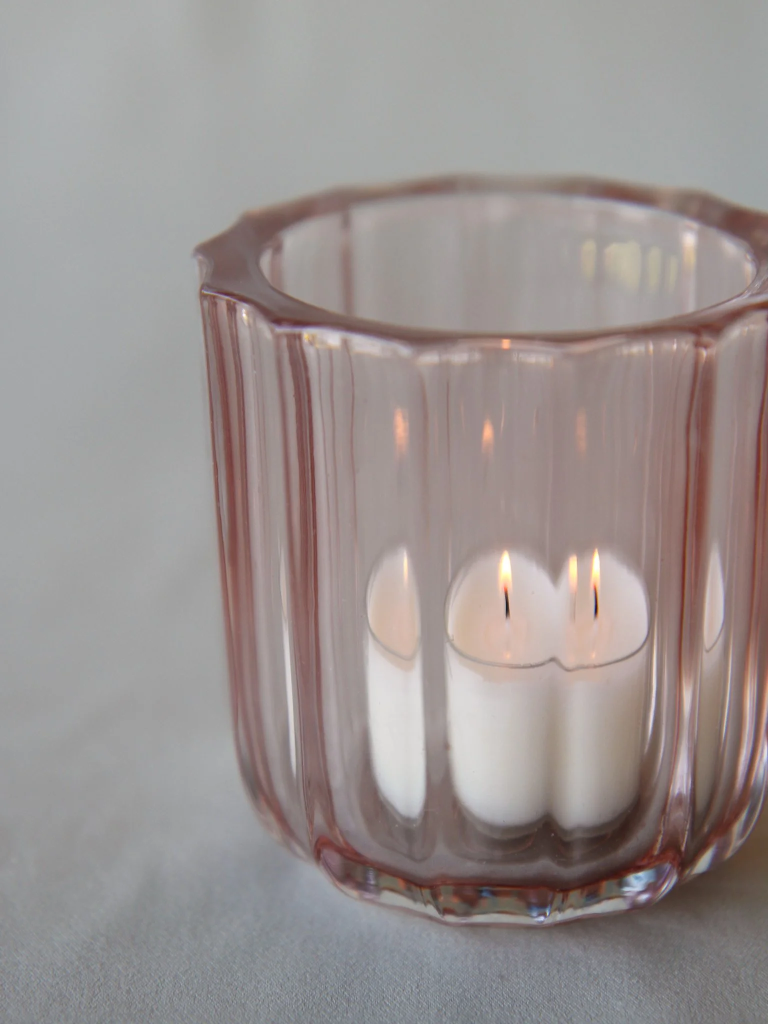 Close-up of a pink glass candle holder with a lit white candle inside, reflecting the flames.