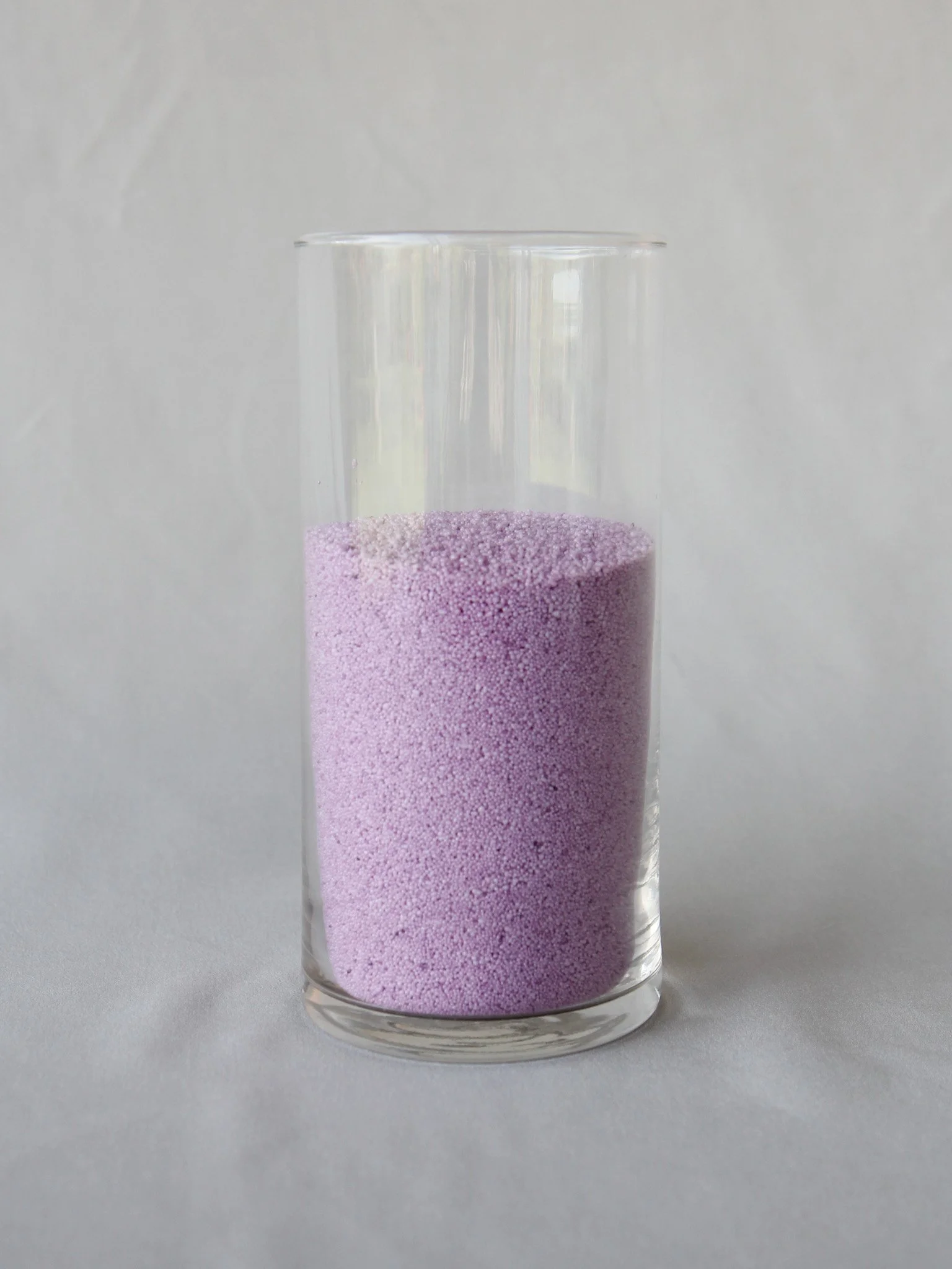 A clear glass filled with purple foam beads.
